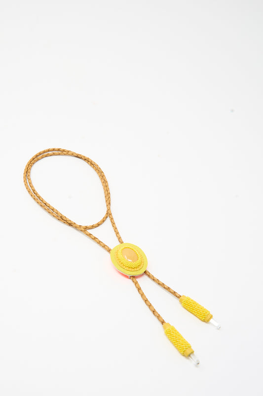 A Robin Mollicone Bolo Necklace in Yellow Calcite featuring an oval-shaped cabochon centerpiece on a braided tan cord with matching yellow cord ends.