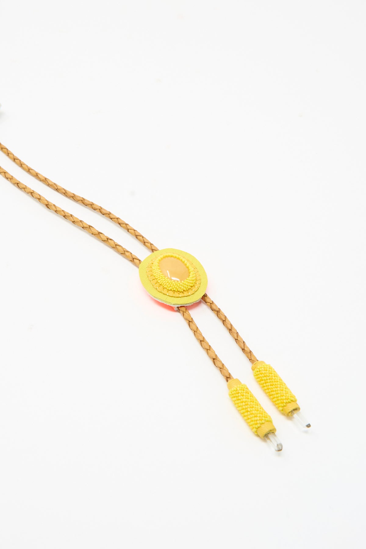 Robin Mollicone Bolo Necklace in Yellow Calcite featuring a pale yellow oval stone on a circular yellow beaded backing, braided tan leather cords, and yellow beaded end caps.