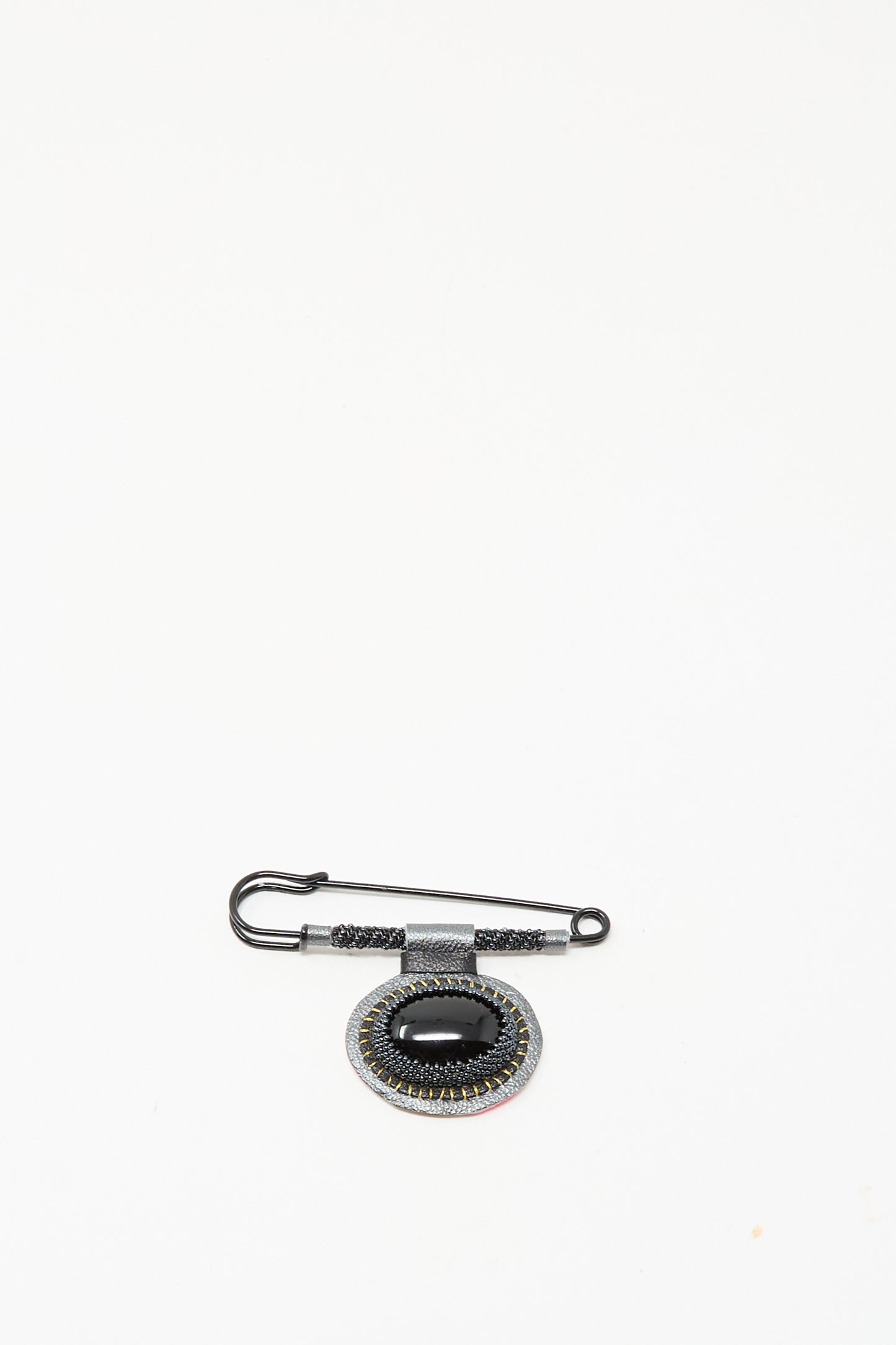 The Robin Mollicone Brooch in Onyx features a black safety pin and an oval pendant with black and silver accents, creating a striking statement against a plain white background.