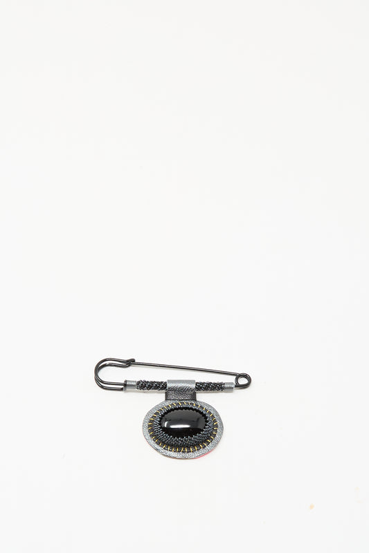 The Robin Mollicone Brooch in Onyx features a black safety pin and an oval pendant with black and silver accents, creating a striking statement against a plain white background.