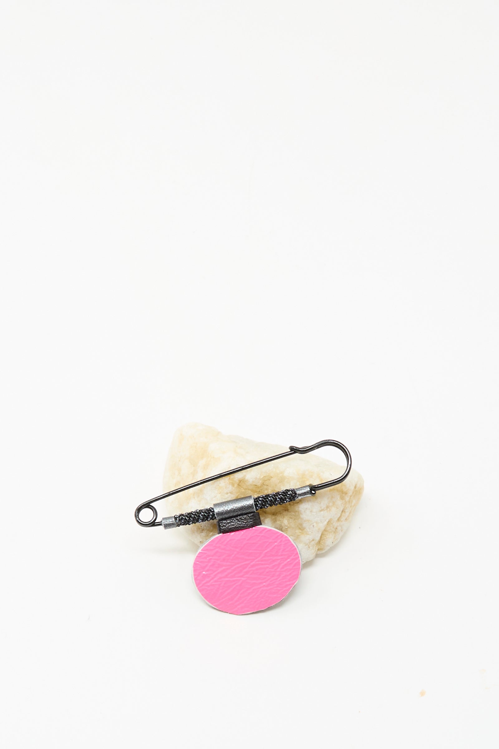The Brooch in Onyx by Robin Mollicone, handmade in NYC, features a textured metal handle and a pink oval tag, shown against pale stone on a white background.