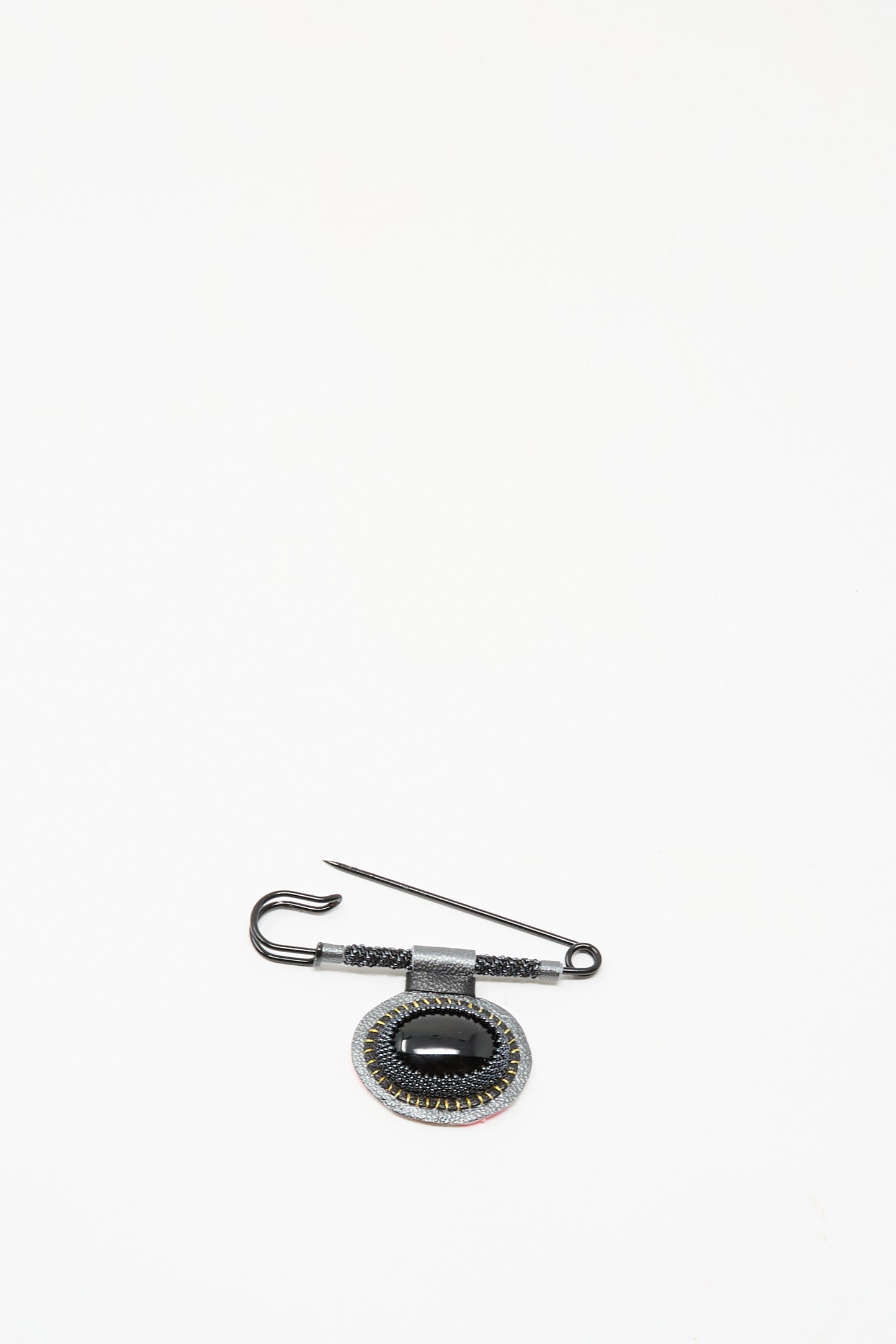 The Brooch in Onyx by Robin Mollicone features a black oval gemstone and intricate detailing, handmade in NYC. This decorative piece is displayed on a plain white background.