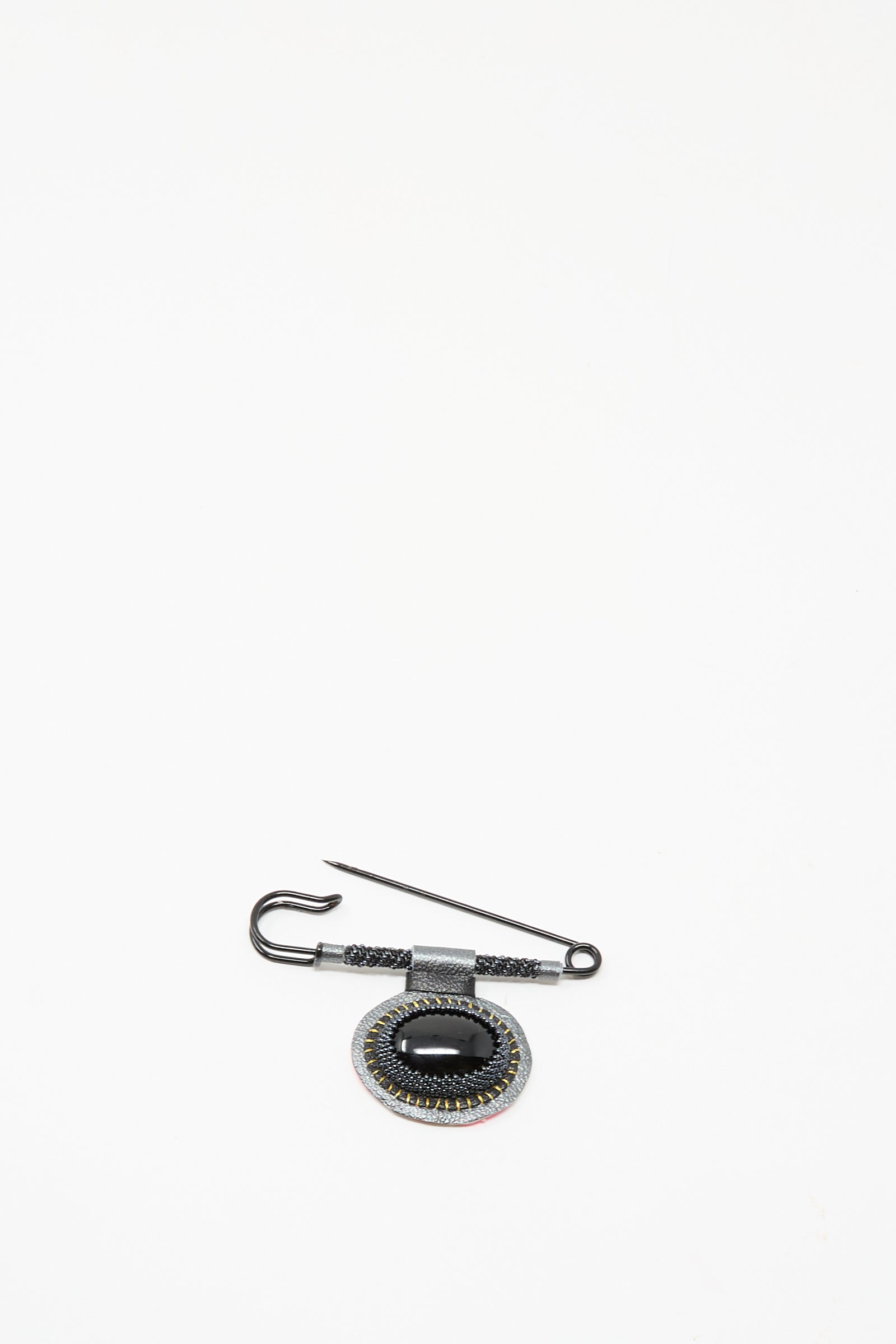 The Brooch in Onyx by Robin Mollicone features a black oval gemstone and intricate detailing, handmade in NYC. This decorative piece is displayed on a plain white background.