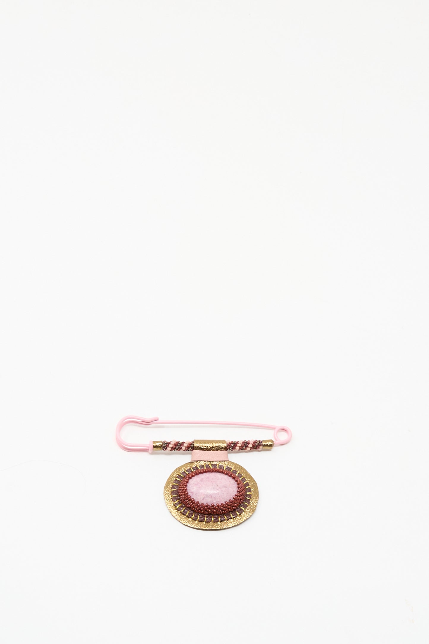 A pink safety pin with beads is displayed next to Robin Mollicone's handmade "Brooch in Rhodonite," featuring gold details, both crafted in NYC and shown on a white background.