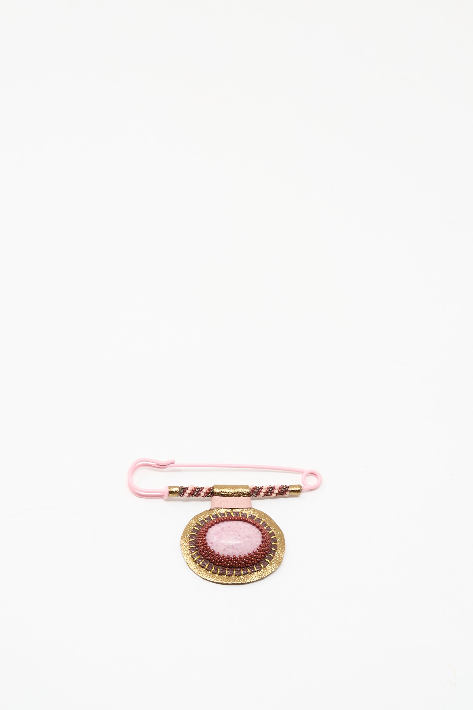 A pink safety pin with beads is displayed next to Robin Mollicone's handmade "Brooch in Rhodonite," featuring gold details, both crafted in NYC and shown on a white background.