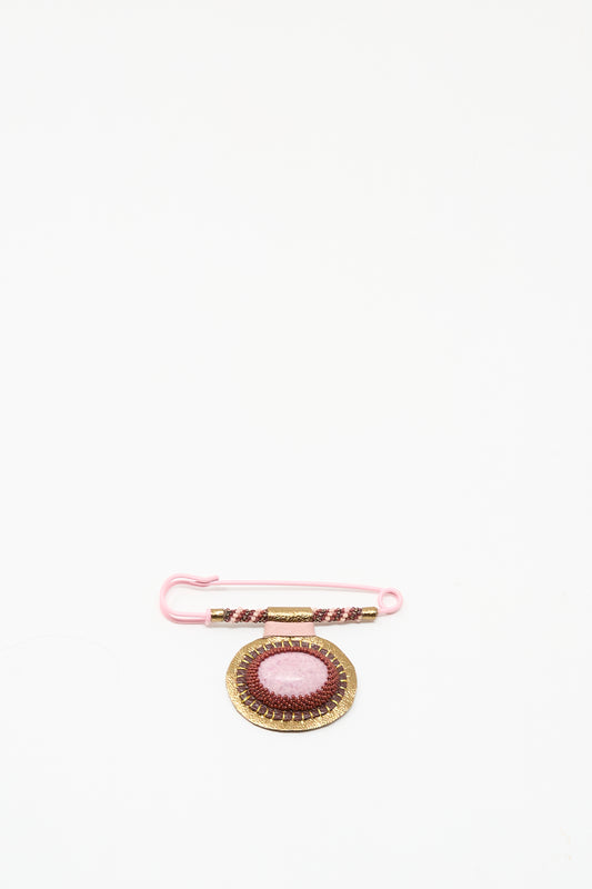 A pink safety pin with beads is displayed next to Robin Mollicone's handmade "Brooch in Rhodonite," featuring gold details, both crafted in NYC and shown on a white background.