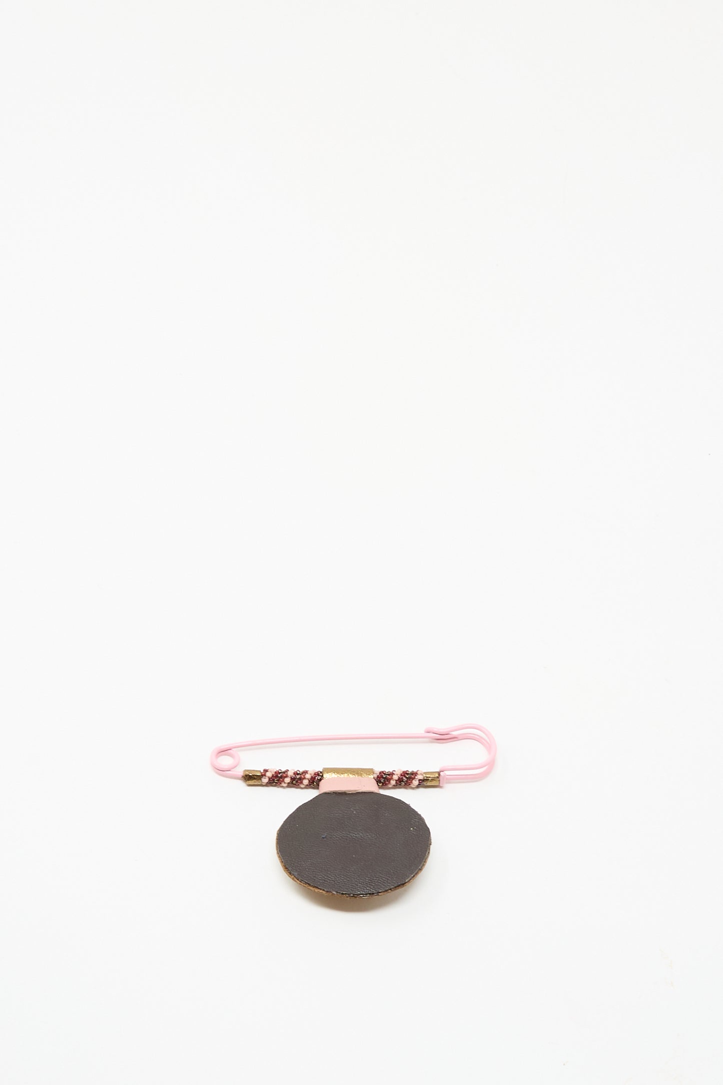 The Brooch in Rhodonite by Robin Mollicone, featuring a round black beaded design on a pink safety pin with a decorated band, is displayed on a white background.