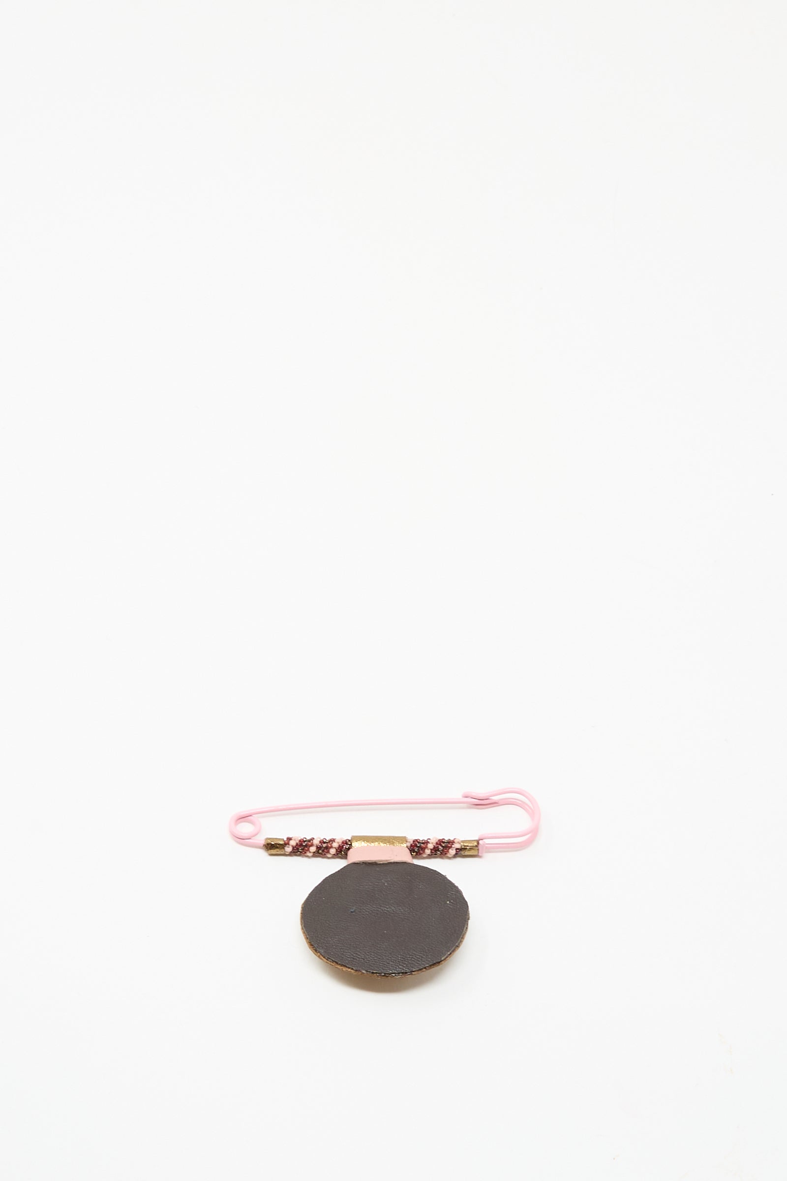The Brooch in Rhodonite by Robin Mollicone, featuring a round black beaded design on a pink safety pin with a decorated band, is displayed on a white background.