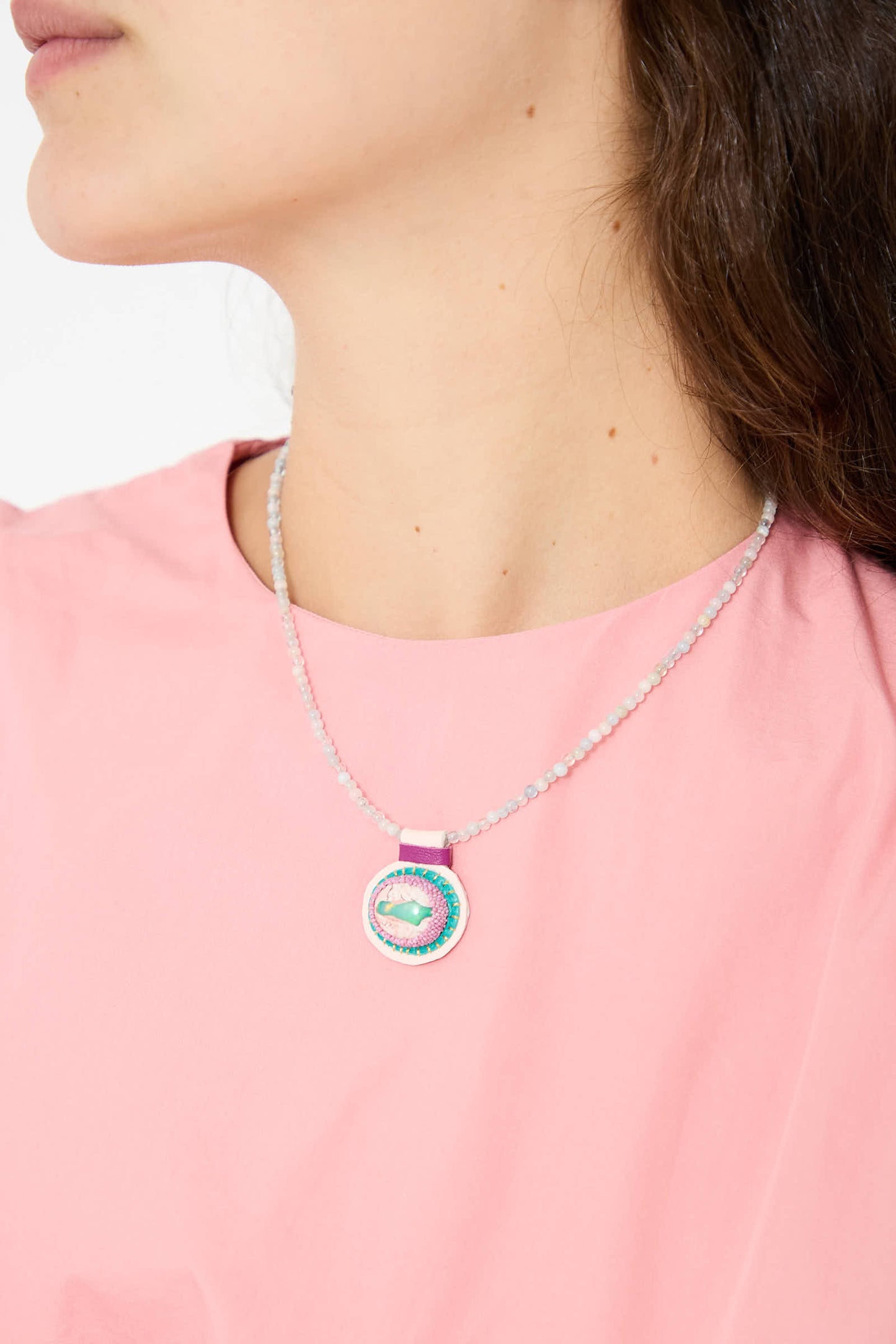 A person wearing a pink shirt is shown from the neck down. They are wearing the Robin Mollicone Charm Necklace in Morganite Beads with Fire Opal Charm.