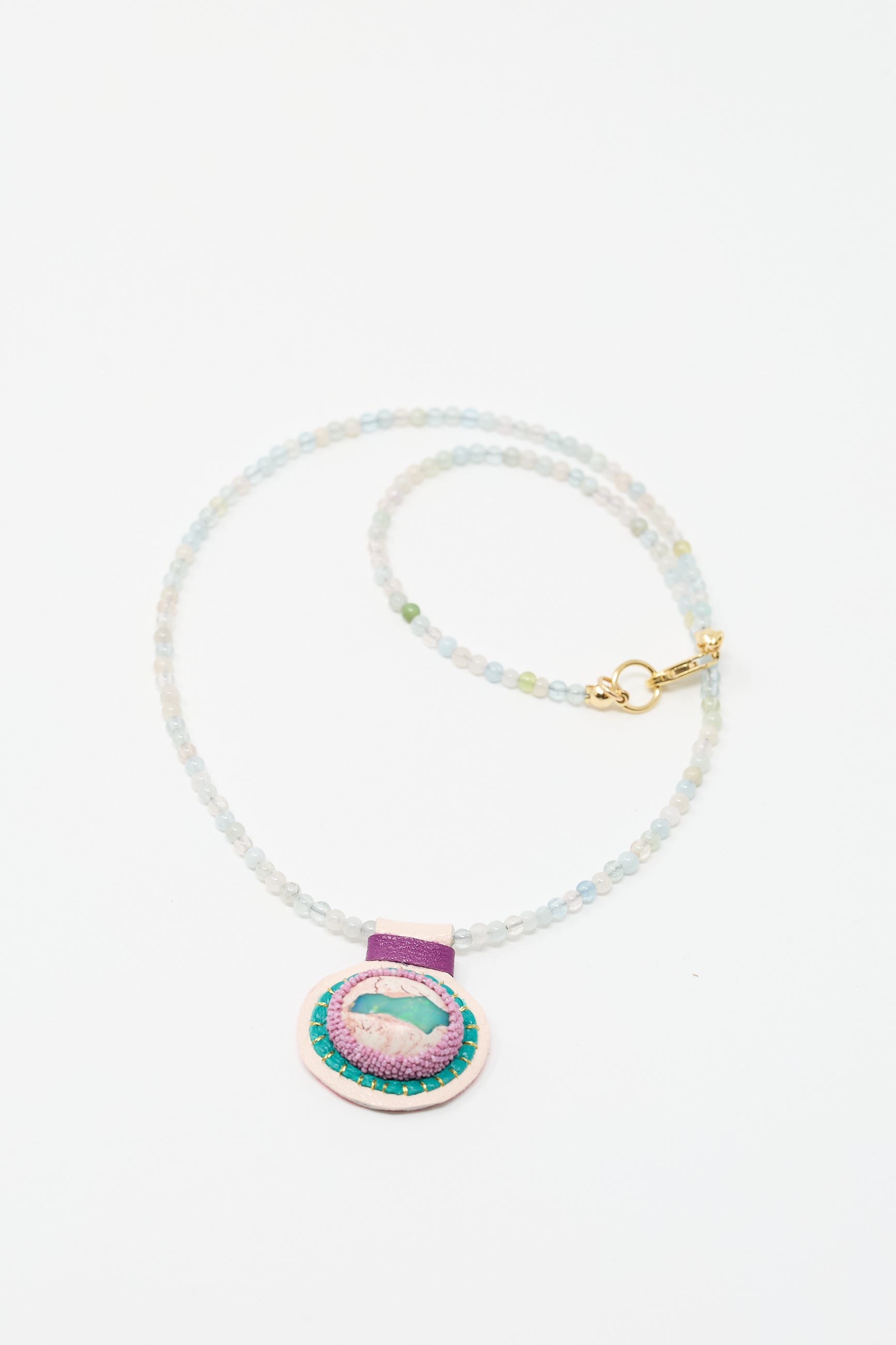 A **Charm Necklace in Morganite Beads with Fire Opal Charm**, featuring morganite beads and a purple and teal circular pendant, by **Robin Mollicone**.