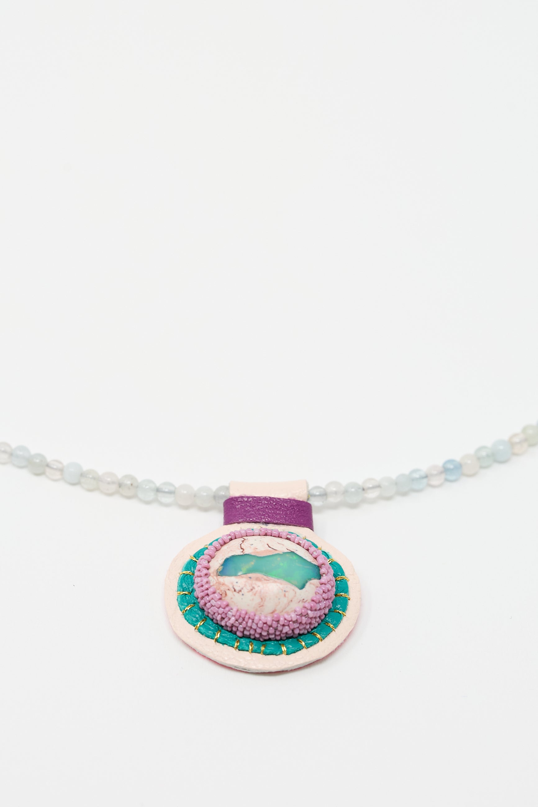 A Charm Necklace in Morganite Beads with Fire Opal Charm by Robin Mollicone adorned with morganite beads and a circular pendant featuring a turquoise stone center and a purple accent on a white background.