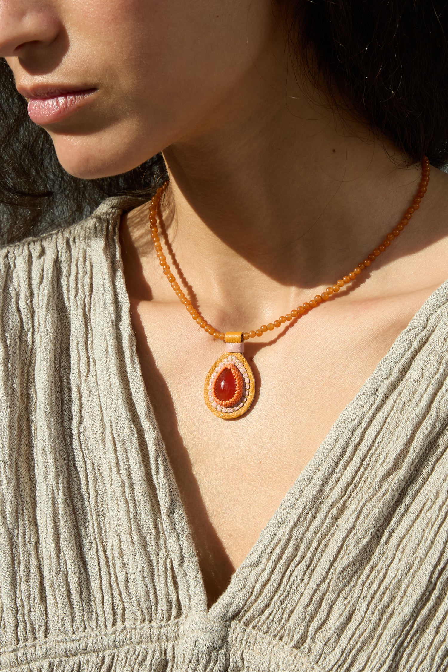 A woman wearing a Robin Mollicone Charm Necklace in Carnelian.