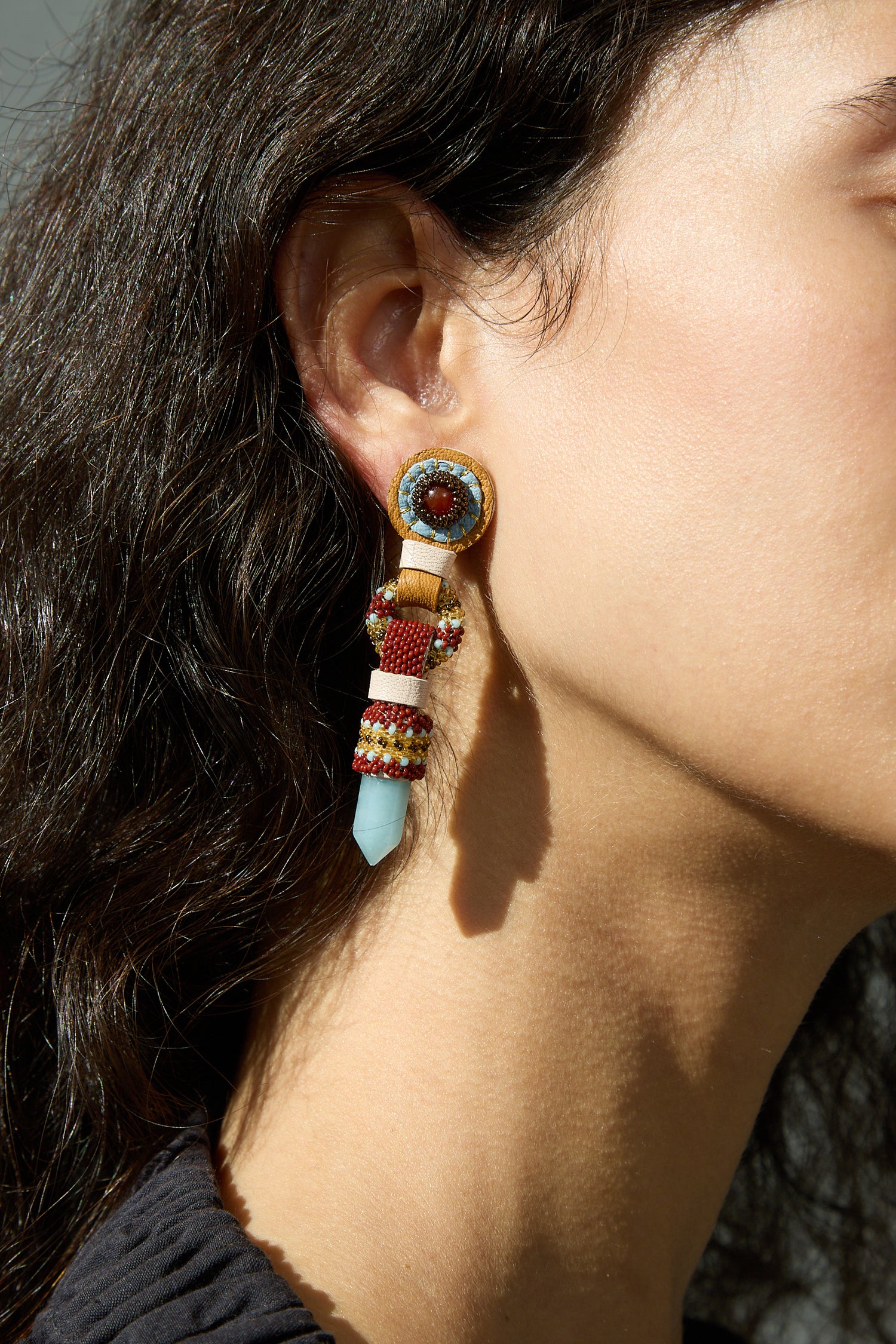 A close up of a woman's ear adorned with Robin Mollicone Crystal Drop Earrings with Carnelian and Aquamarine.