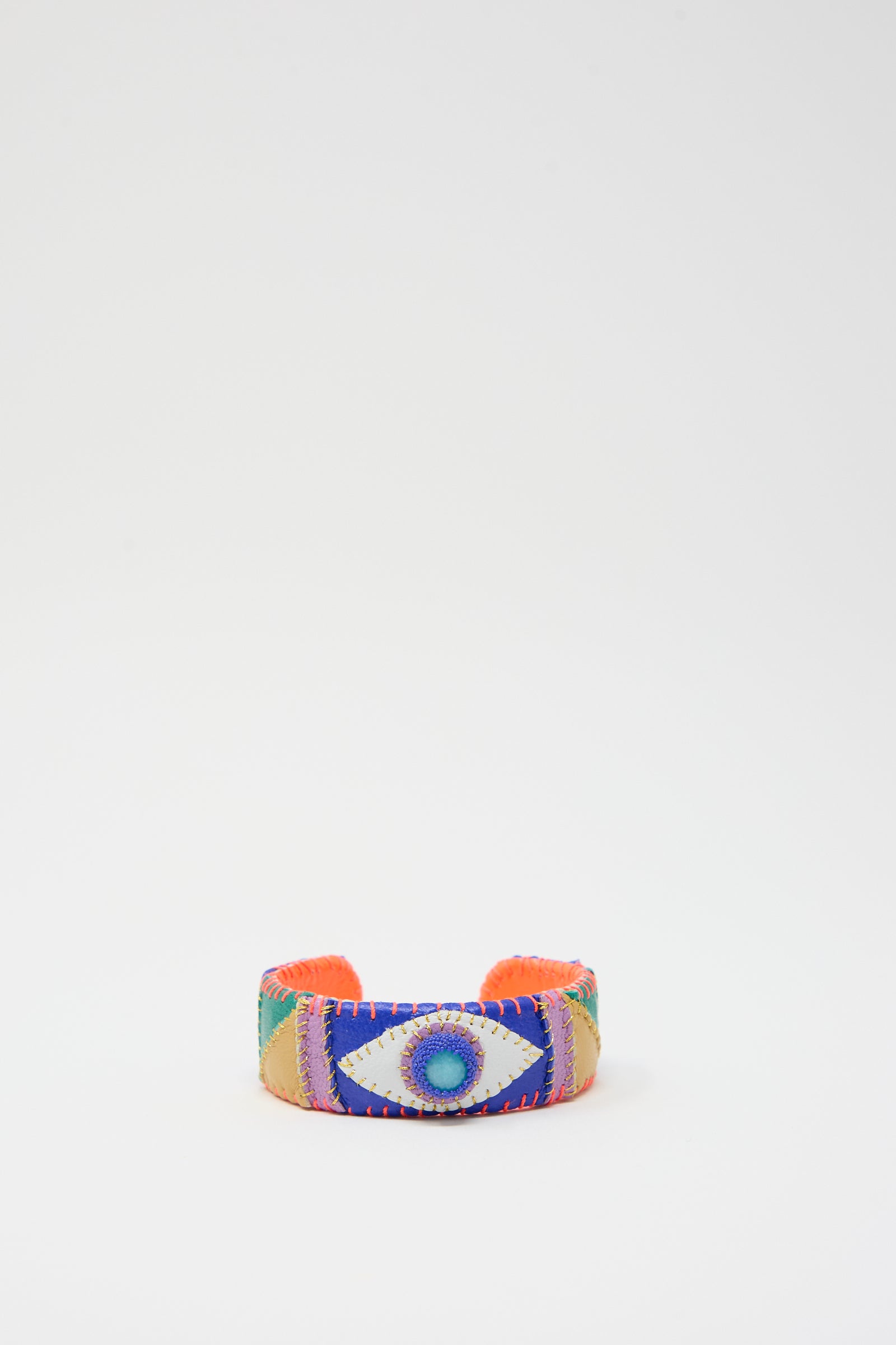 The "Eye Cuff in Amazonite" by Robin Mollicone is a vibrant bracelet showcasing a central amazonite eye design, set against a sleek white background and enhanced with intricate patchwork leather detailing.