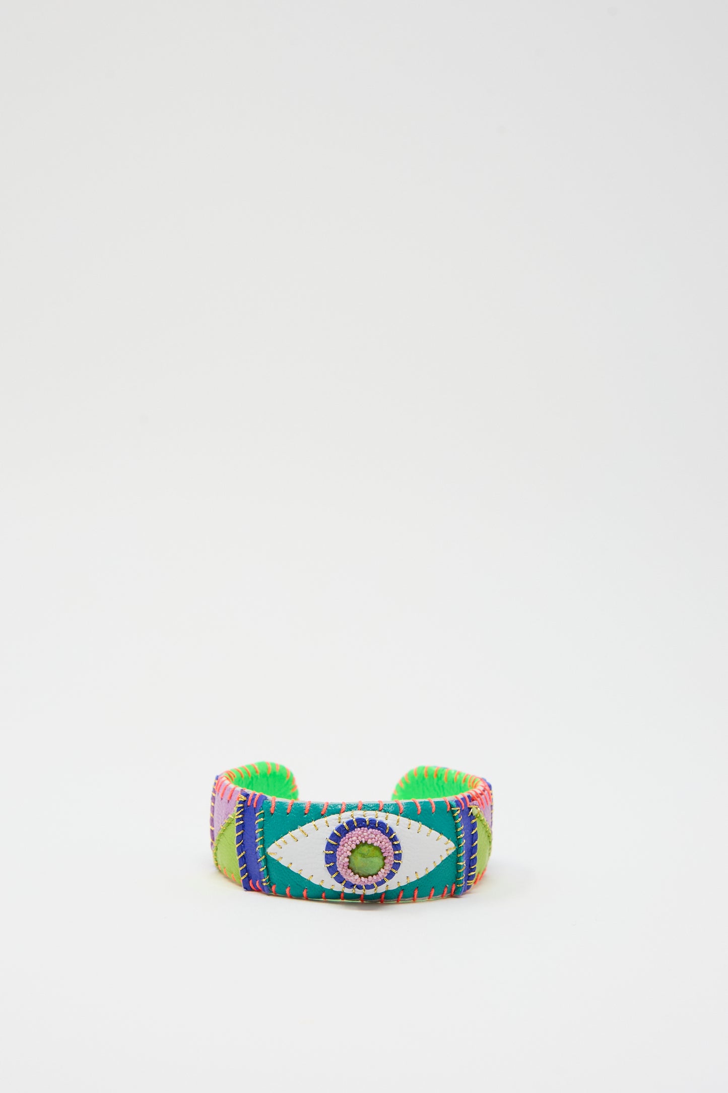 The Eye Cuff in Green Turquoise by Robin Mollicone is a vibrant, wide fabric bracelet with an embroidered green turquoise eye design at its center, surrounded by multicolored stitching patterns. Handmade in New York, it features a plain white background.