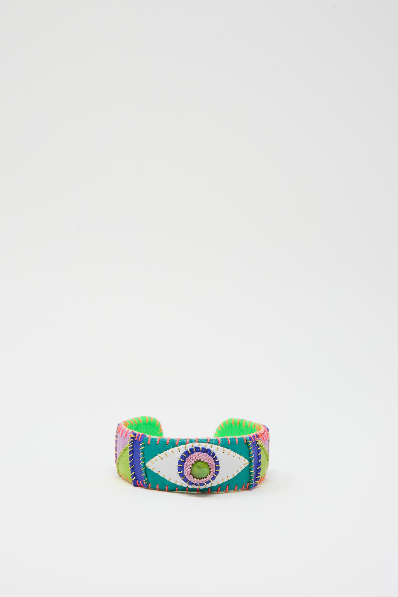 The Eye Cuff in Green Turquoise by Robin Mollicone is a vibrant, wide fabric bracelet with an embroidered green turquoise eye design at its center, surrounded by multicolored stitching patterns. Handmade in New York, it features a plain white background.