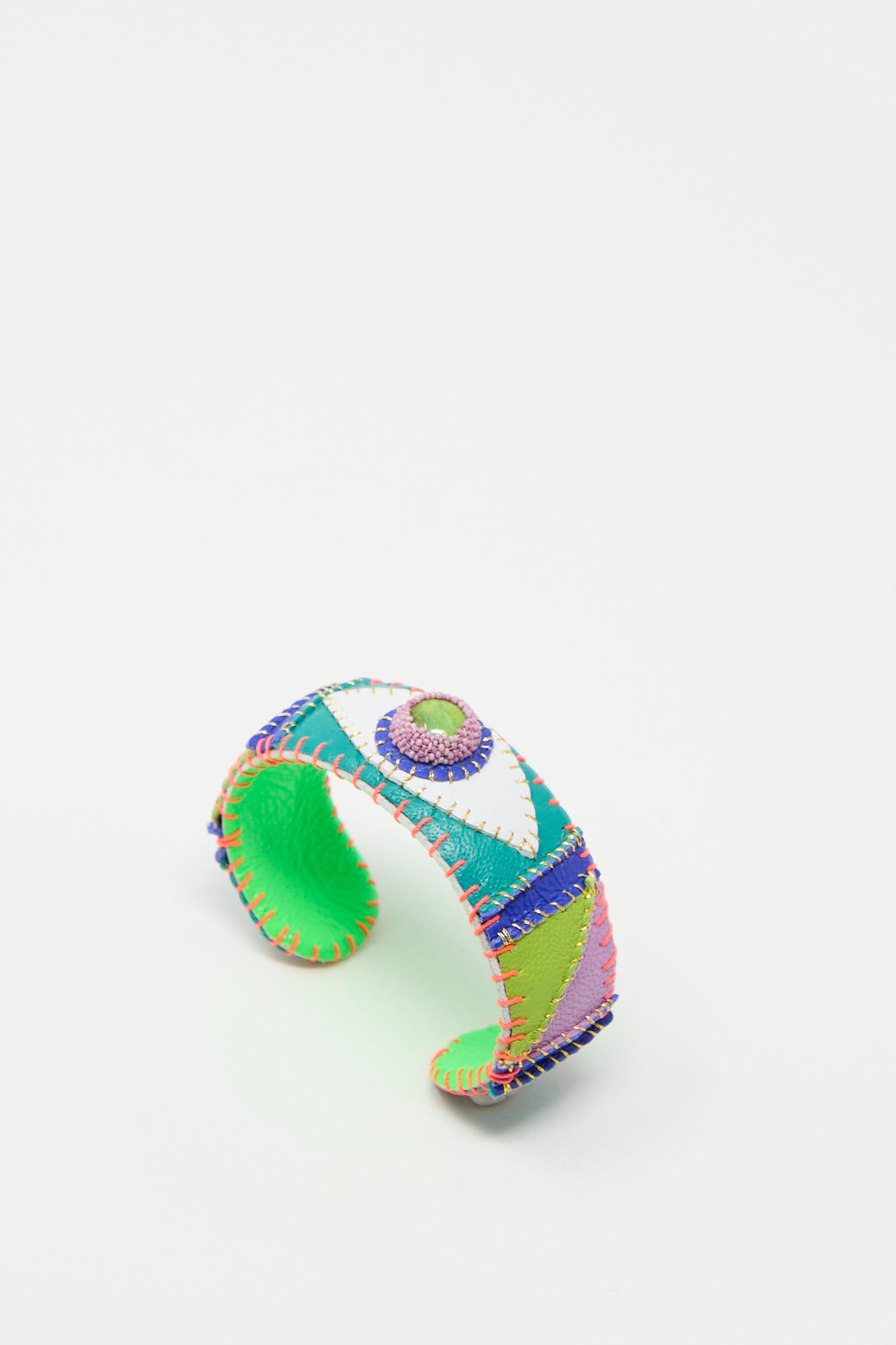 The Eye Cuff in Green Turquoise by Robin Mollicone is a handmade, multicolored bracelet crafted in New York. It features a patchwork design with detailed stitching and a large central bead. The interior of the bracelet is green.