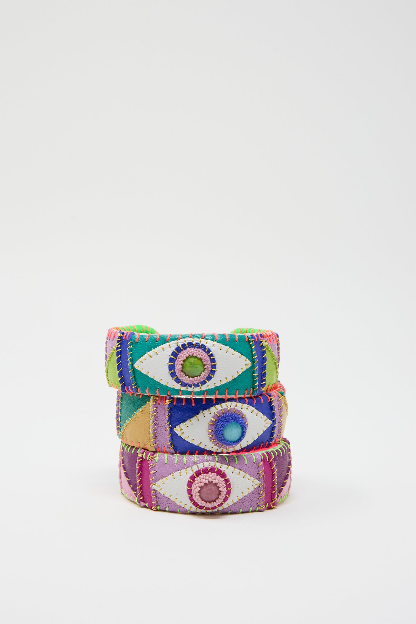 The Eye Cuff in Green Turquoise by Robin Mollicone features three vibrant fabric bracelets adorned with green turquoise eye designs, expertly handmade in New York and beautifully showcased against a white background.