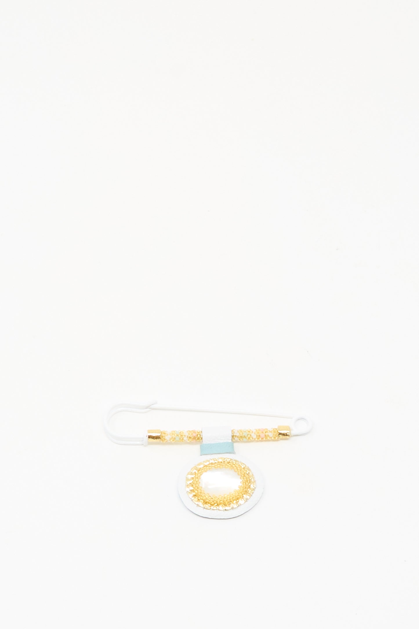 The Gem Drop Brooch in Mother of Pearl by Robin Mollicone features gold and white beads with a circular Mother of Pearl pendant, displayed on a plain white background.