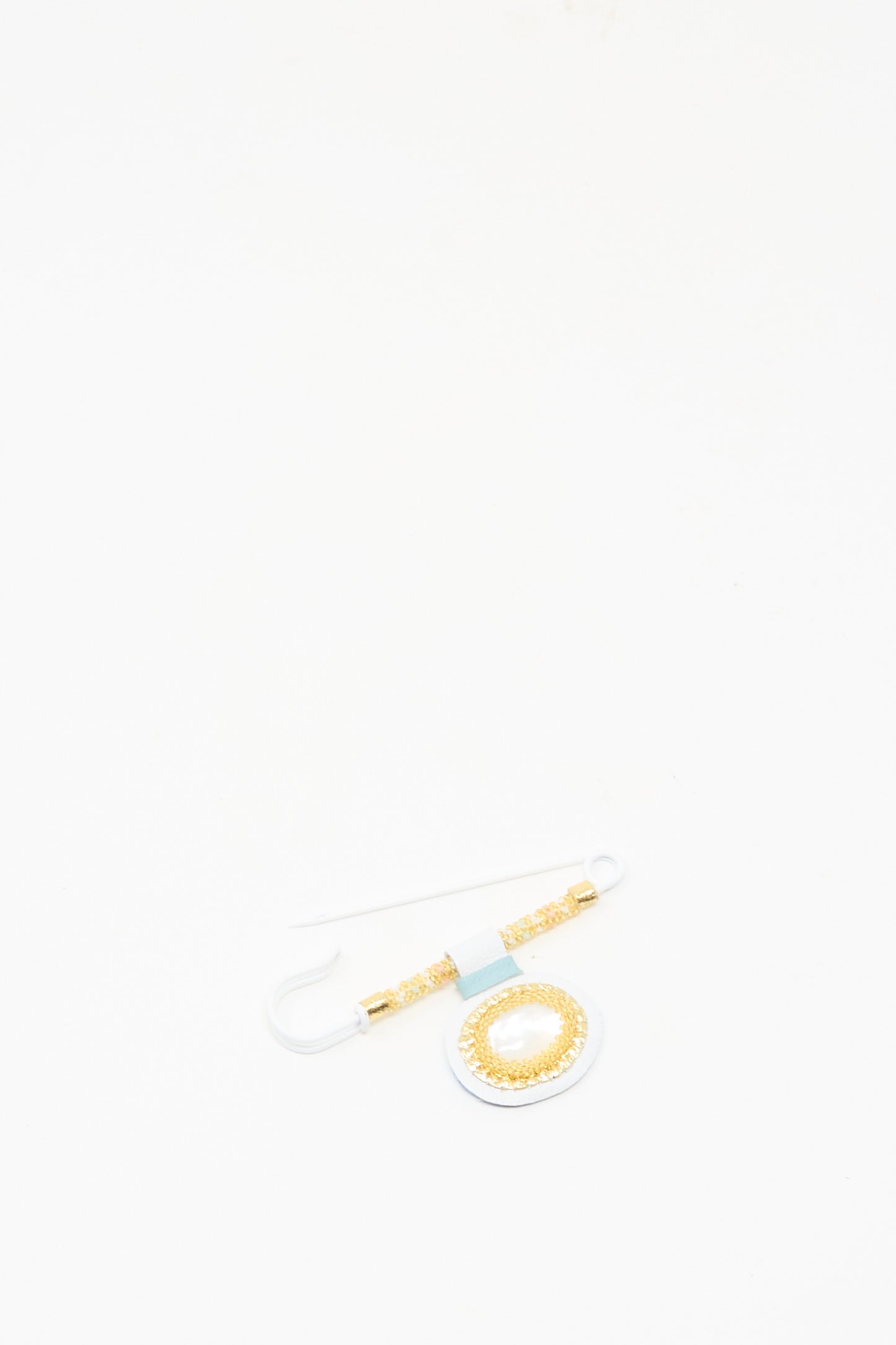 The Gem Drop Brooch in Mother of Pearl by Robin Mollicone, featuring a circular gold and white design with Mother of Pearl accents, is displayed on a white background.