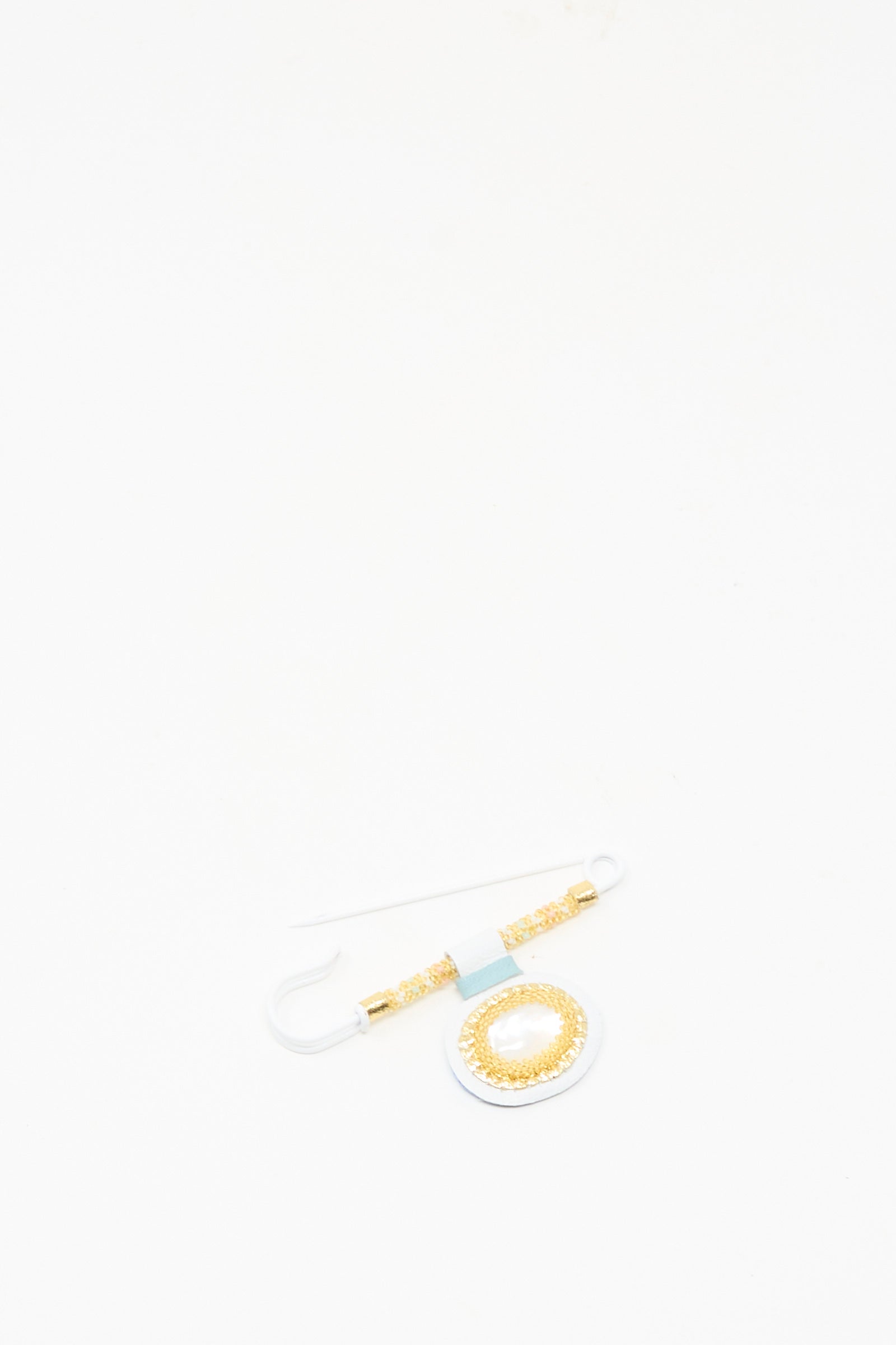 The Gem Drop Brooch in Mother of Pearl by Robin Mollicone, featuring a circular gold and white design with Mother of Pearl accents, is displayed on a white background.