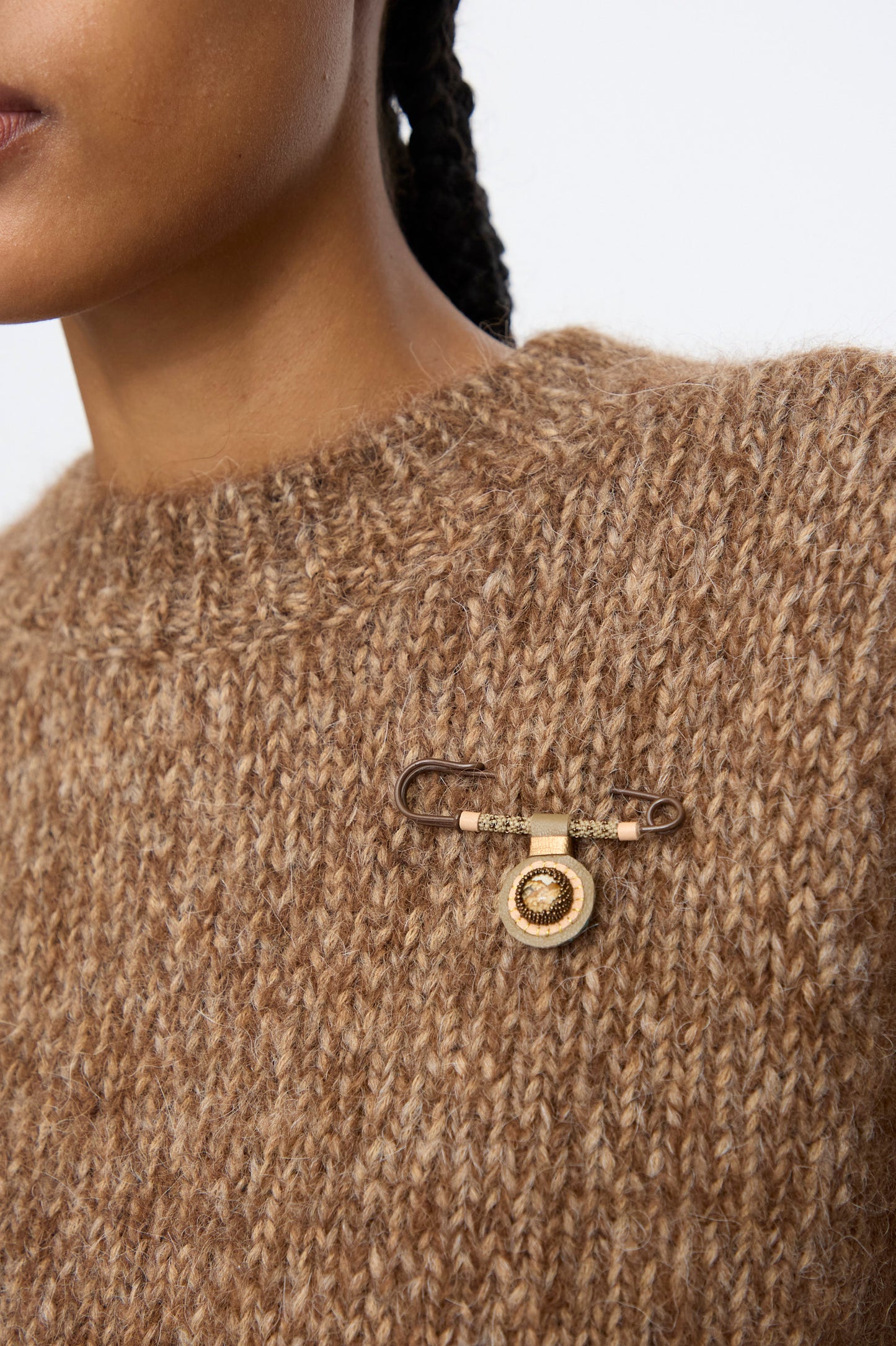 A person wears the Robin Mollicone Gem Drop Safety Pin in Brown with Picture Jasper—a large handmade NYC brooch—on the left side of their brown textured sweater.