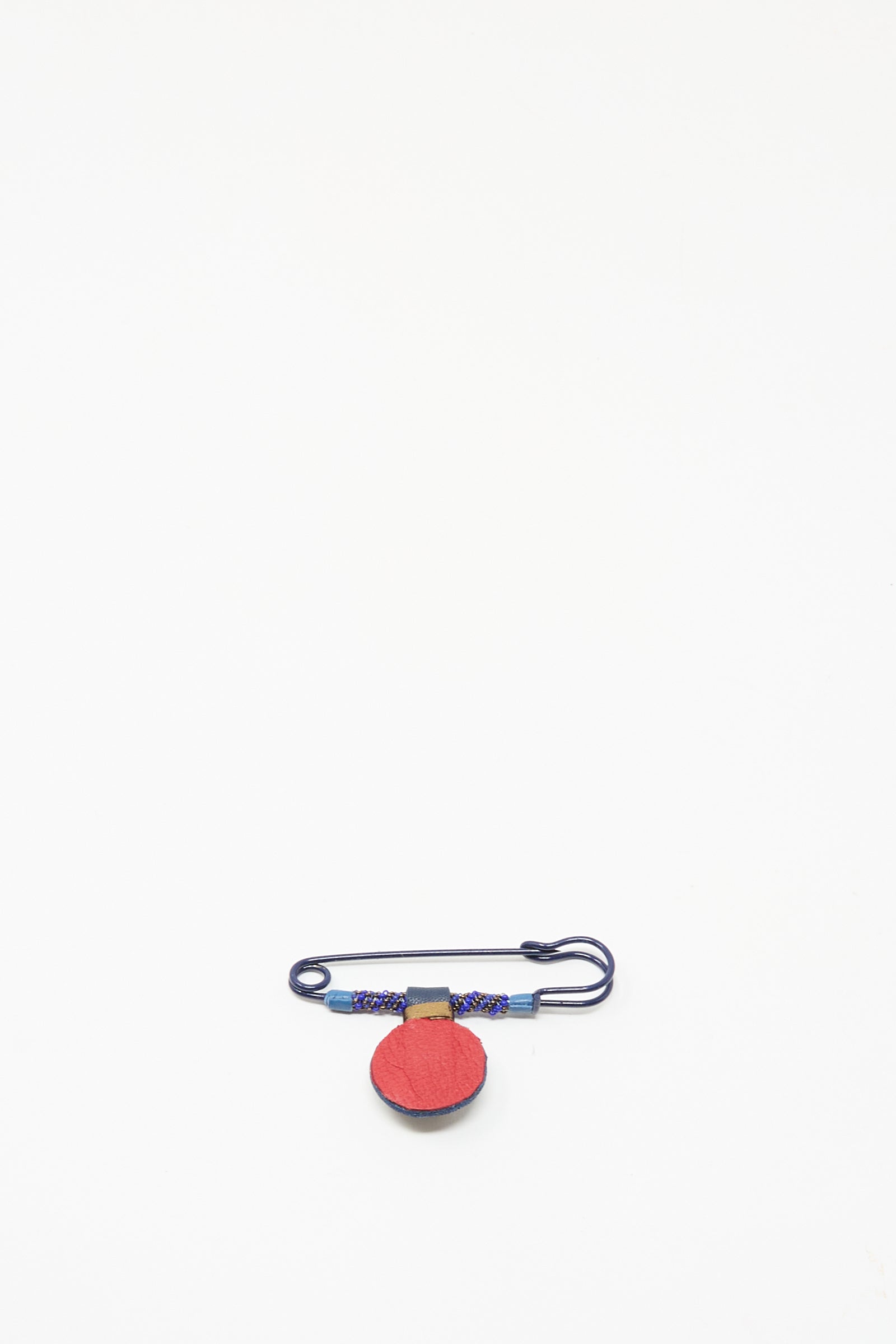The Gem Drop Safety Pin in Lapis by Robin Mollicone is a handmade beaded safety pin featuring blue and red thread and a small red fabric circle, crafted in NYC and shown on a plain white background.