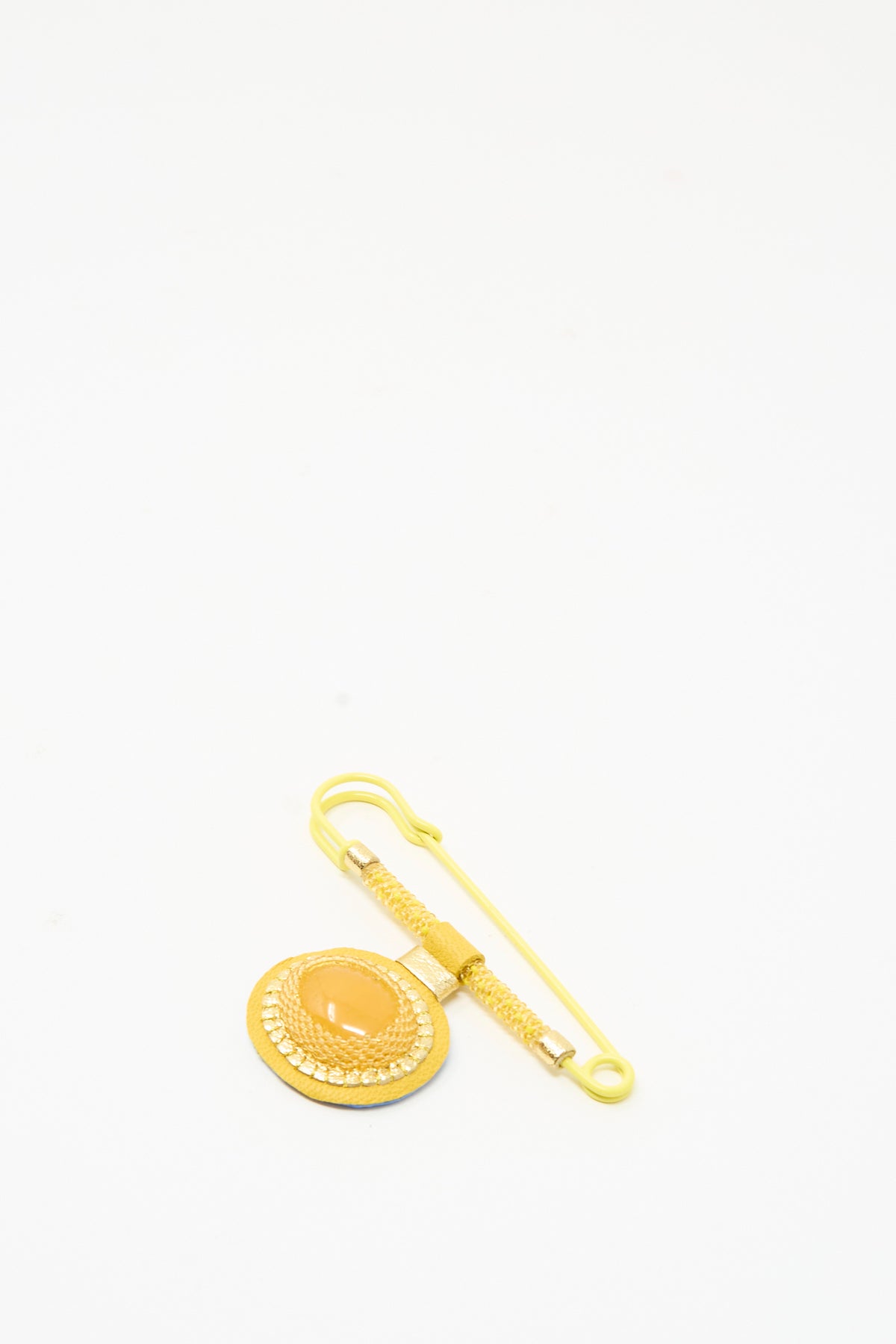 A Robin Mollicone Gem Drop Safety Pin in Yellow Calcite, featuring a circular ornament with a central amber-toned cabochon attached to a safety pin.