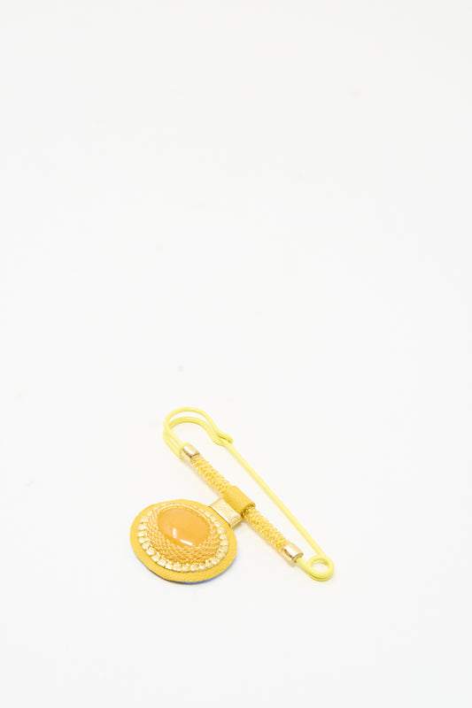 A Robin Mollicone Gem Drop Safety Pin in Yellow Calcite, featuring a circular ornament with a central amber-toned cabochon attached to a safety pin.
