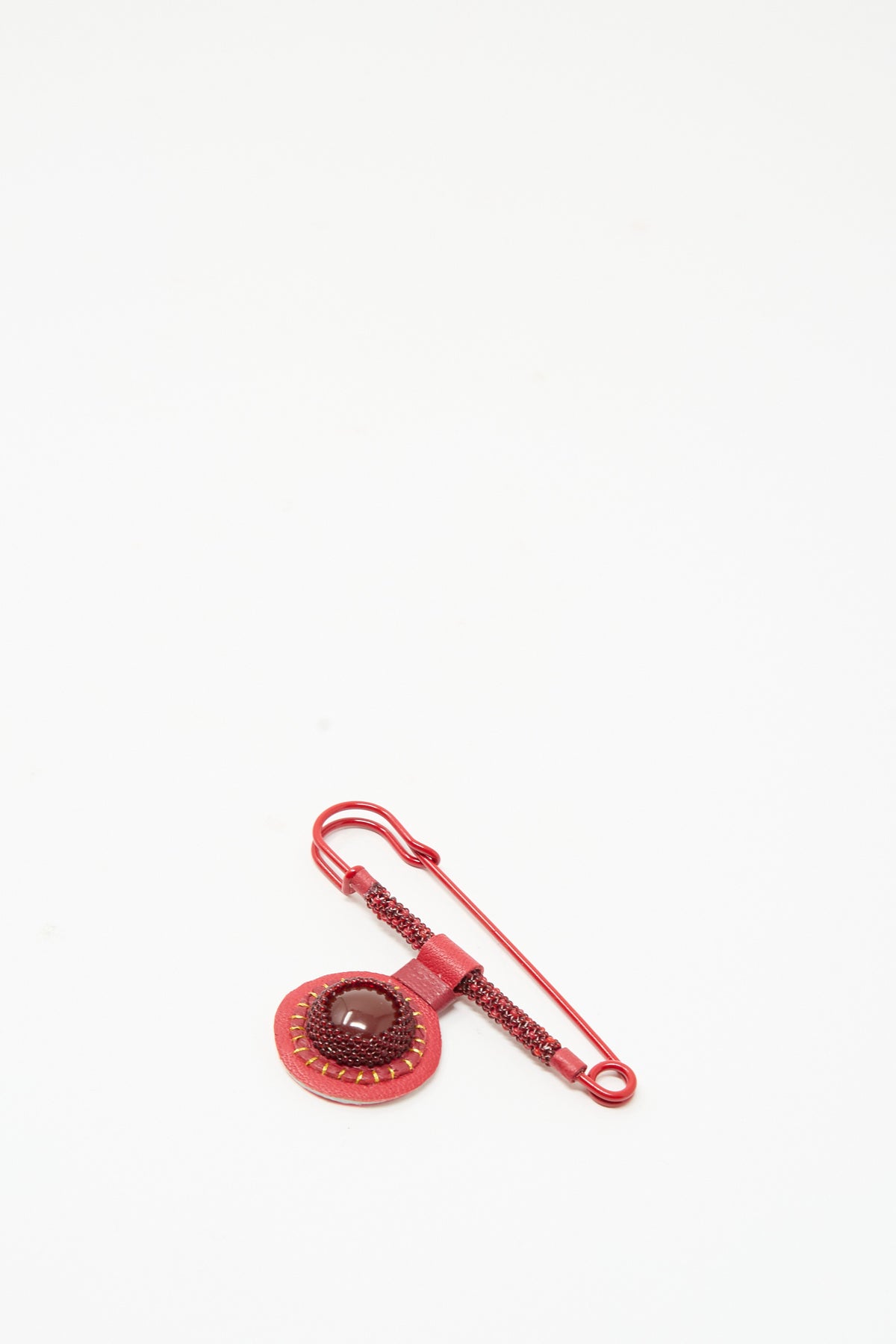 A Gem Safety Pin in Red Carnelian featuring a circular, handmade in New York beaded brooch with a dark red cabochon stone surrounded by beadwork.