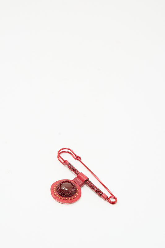 A Gem Safety Pin in Red Carnelian featuring a circular, handmade in New York beaded brooch with a dark red cabochon stone surrounded by beadwork.