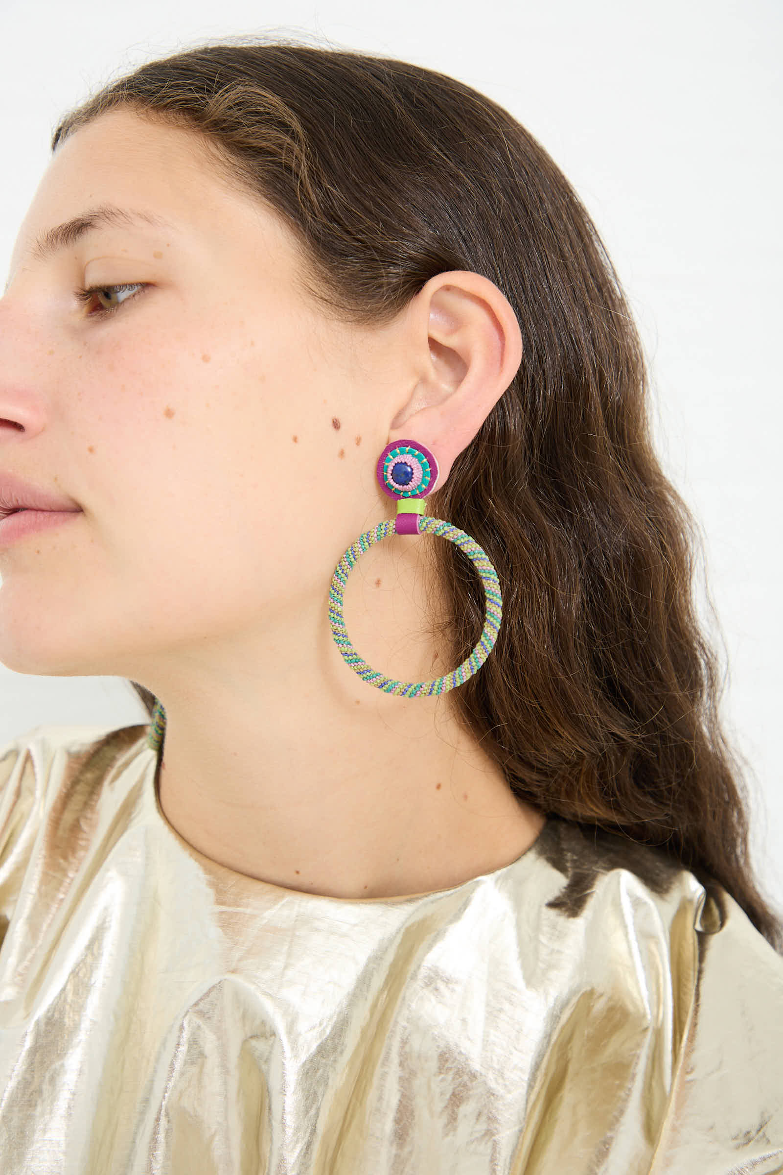 A person with long dark hair wears a pair of Robin Mollicone Large Beaded Hoop Earrings in Multi Spiral with Lapis Stone Tops, elegantly complemented by sterling silver posts, made in New York.