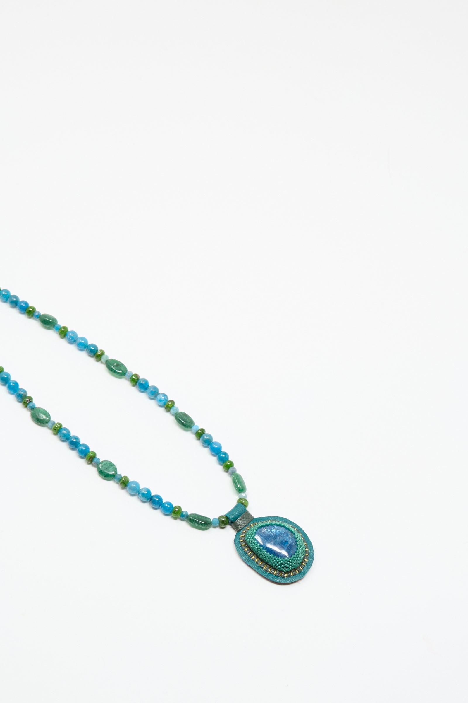 The Love Bead Charm Necklace in Blue with Apatite Charm by Robin Mollicone features vintage blue and green glass beads and a large oval apatite pendant, displayed on a white background.