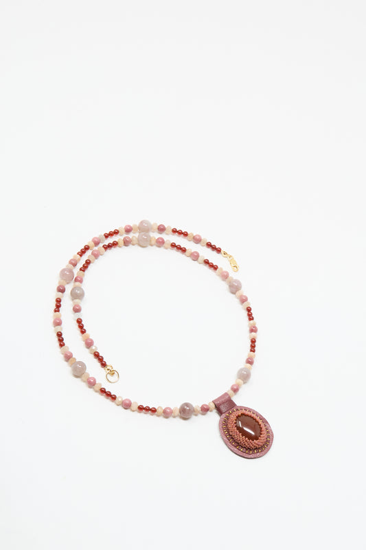 The Robin Mollicone Love Bead Necklace in Pink with Carnelian Charm features alternating pink and red vintage glass beads and a round pink pendant with a central oval stone, shown on a white background.