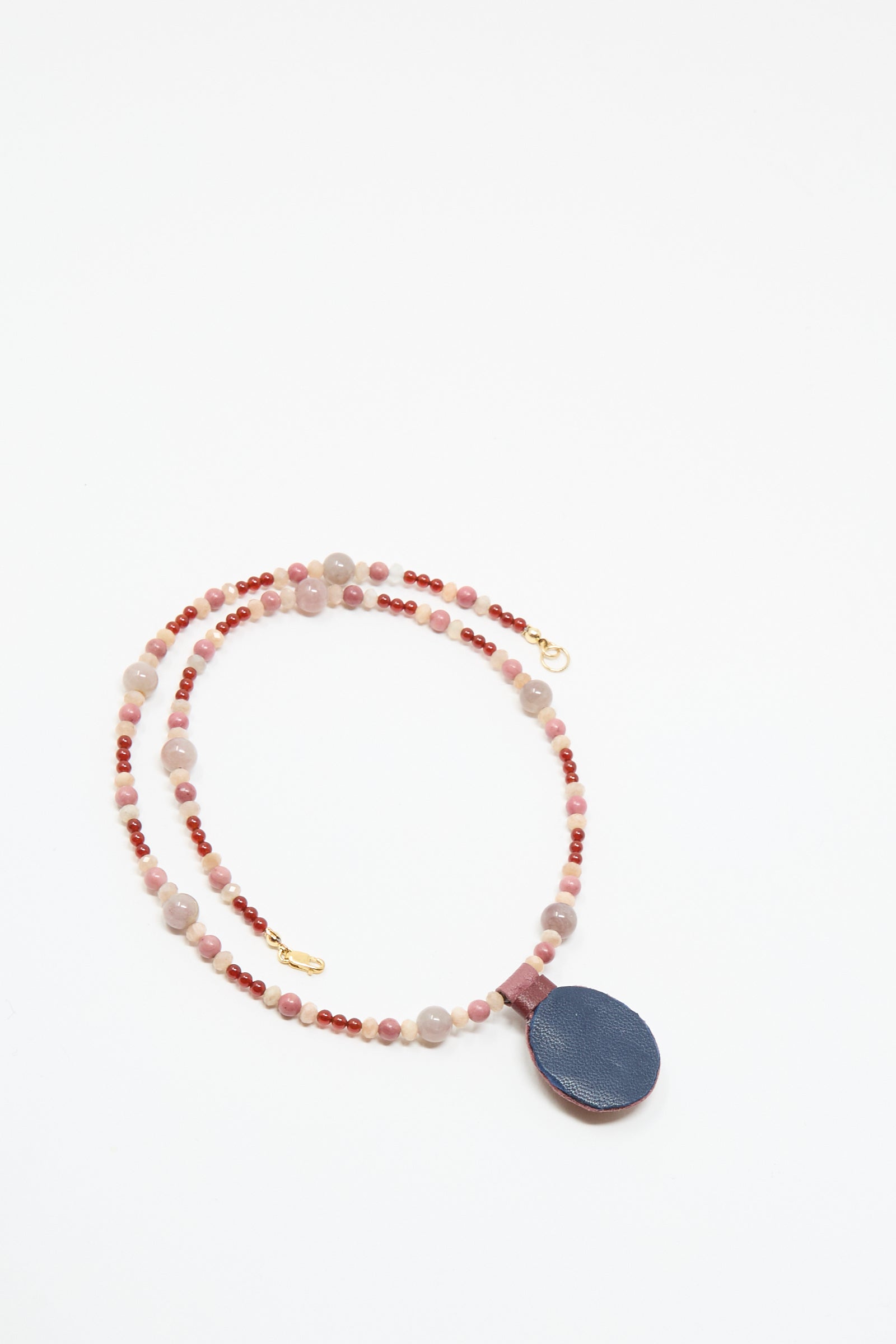 The Robin Mollicone Love Bead Necklace in Pink with Carnelian Charm features vintage pink and red glass beads, a large round dark blue pendant, and gold clasp, displayed on a white background.