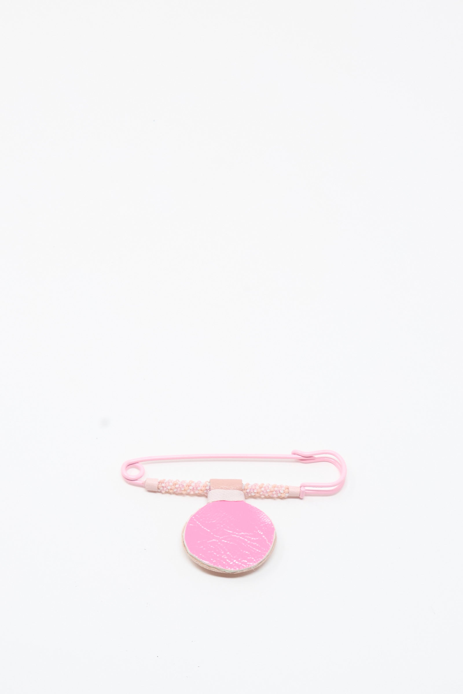 The Moonstone Gem Drop Brooch in Pink by Robin Mollicone is displayed on a plain white background, featuring delicate beaded safety pin detailing and a textured, circular pink tag—all handmade in NYC.