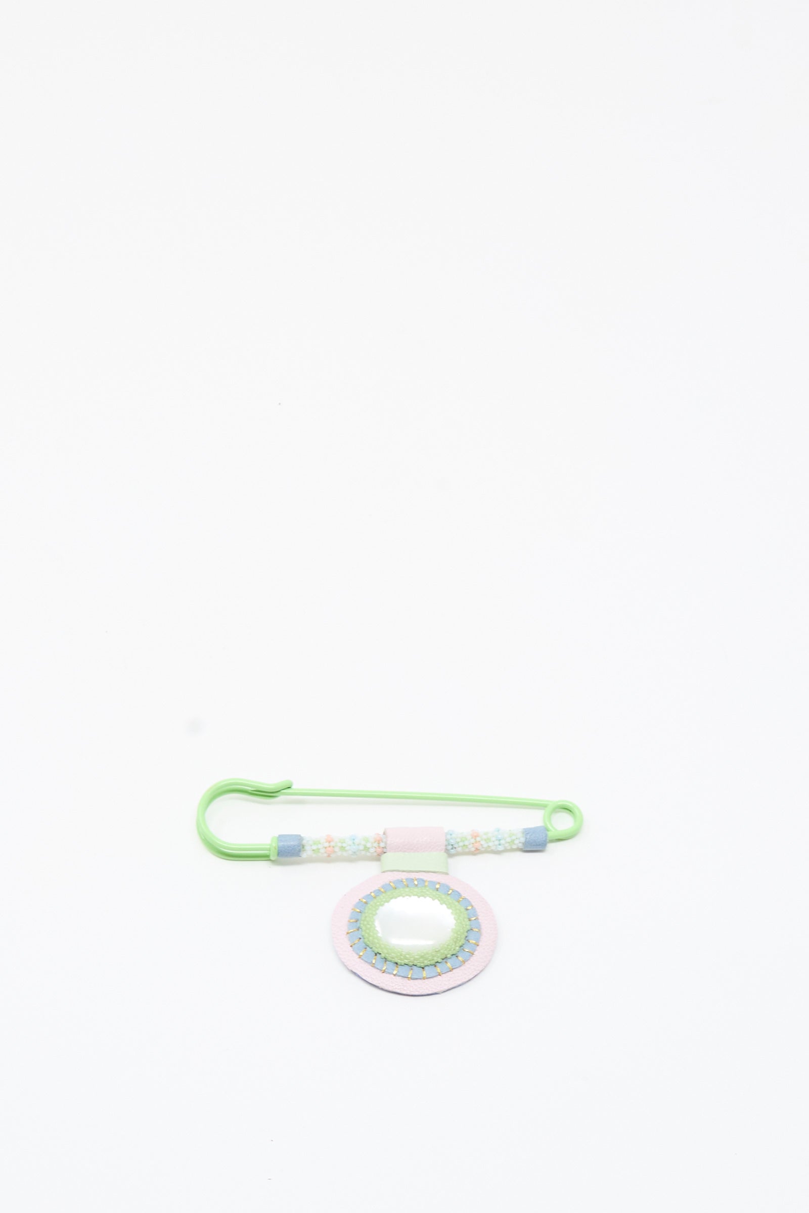 The Mother of Pearl Gem Drop Brooch in Pink, Blue, and Green by Robin Mollicone features pastel beads and a round Mother of Pearl ornament on a safety pin, beautifully handmade in NYC and displayed on a white background.