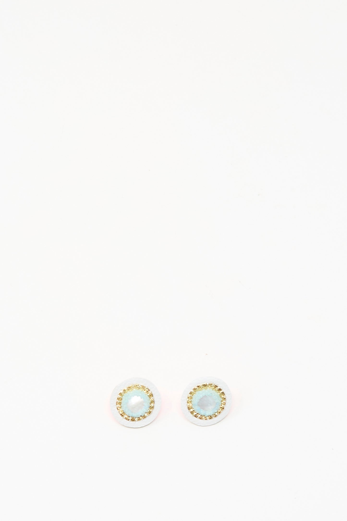 Robin Mollicone Stud Earrings in Mother of Pearl feature light blue stones at the center, encircled by a gold-colored border, and are shown on a white background.