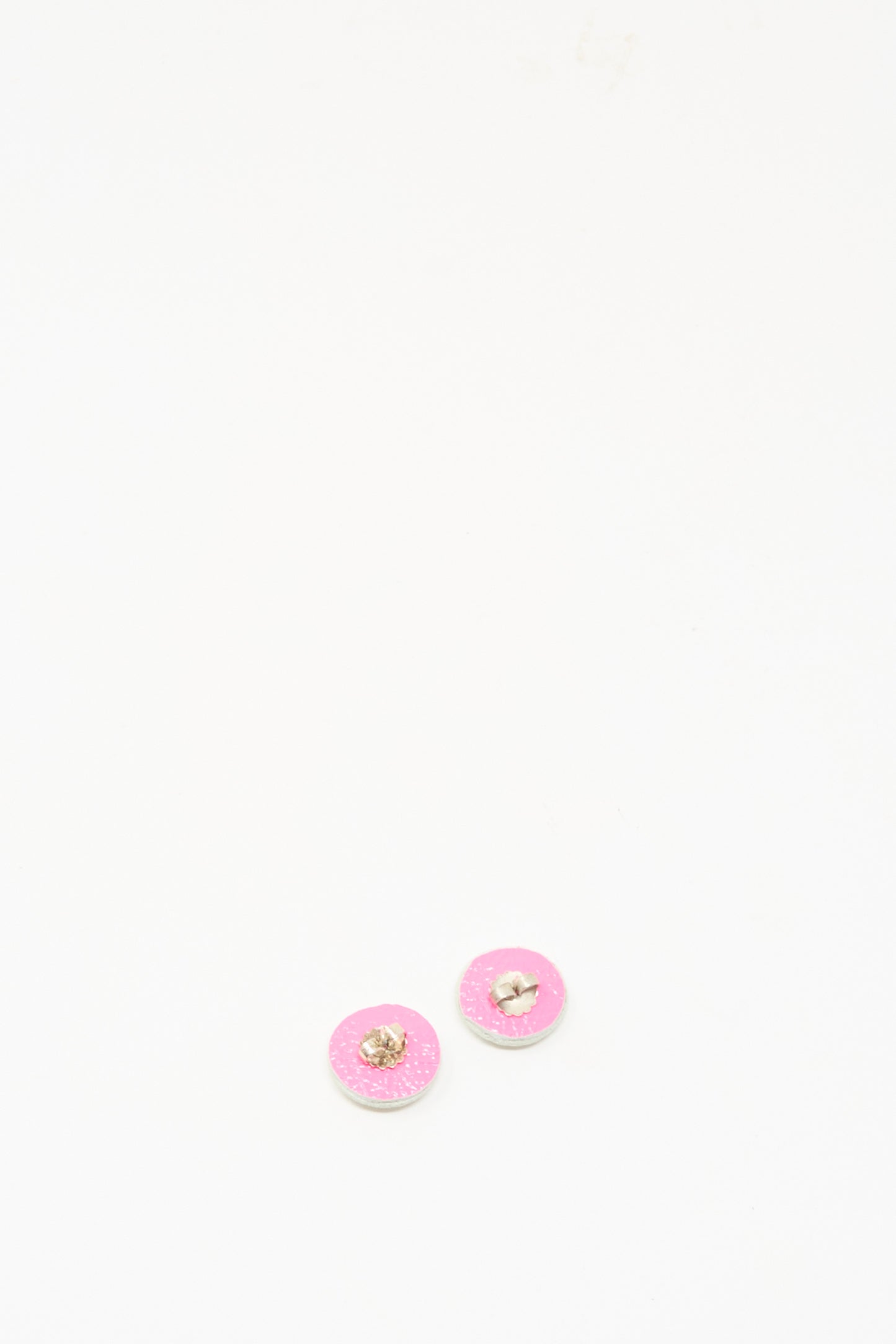 Two small stud earrings in mother of pearl by Robin Mollicone, featuring silver edges and a delicate pink hue, rest on a plain white surface, evoking exquisite handmade craftsmanship.