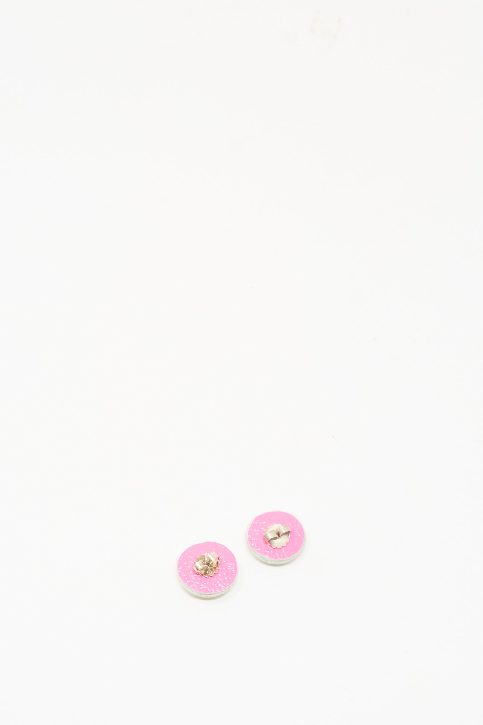 Two small stud earrings in mother of pearl by Robin Mollicone, featuring silver edges and a delicate pink hue, rest on a plain white surface, evoking exquisite handmade craftsmanship.