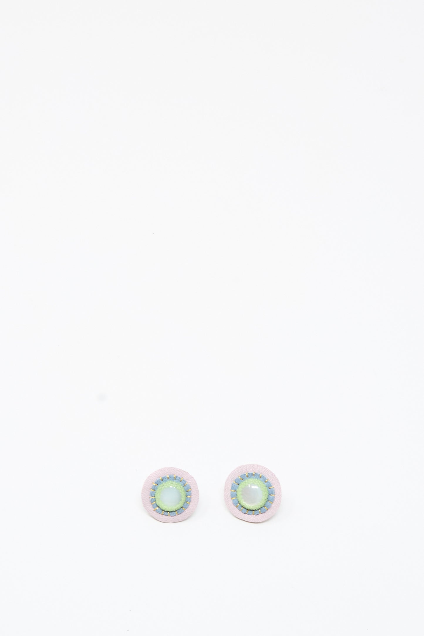 A pair of handmade Robin Mollicone Mother of Pearl Stud Earrings in Blue and Green, featuring round, iridescent green and blue centers with light-colored borders, displayed on a plain white background.