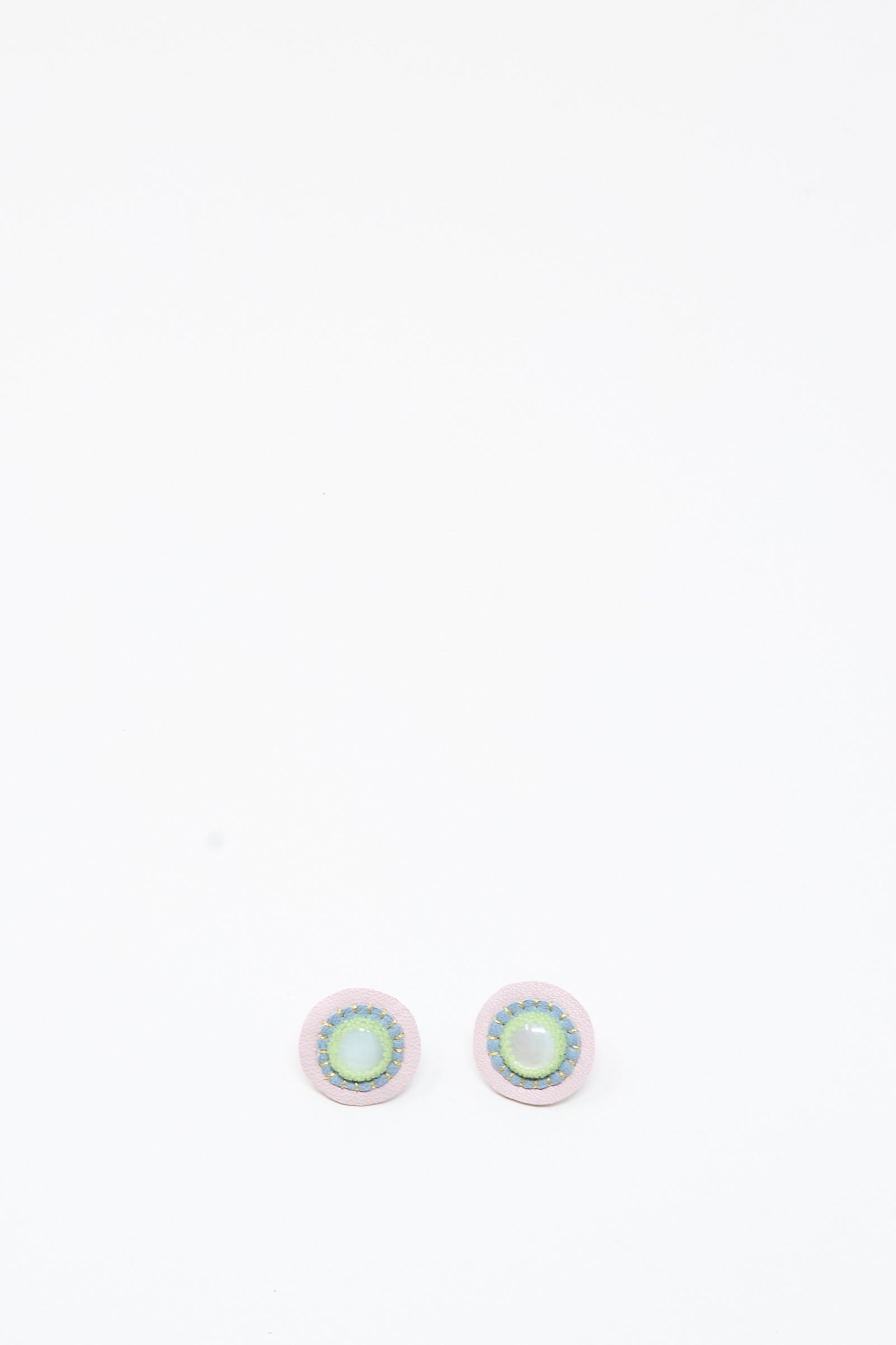 A pair of handmade Robin Mollicone Mother of Pearl Stud Earrings in Blue and Green, featuring round, iridescent green and blue centers with light-colored borders, displayed on a plain white background.