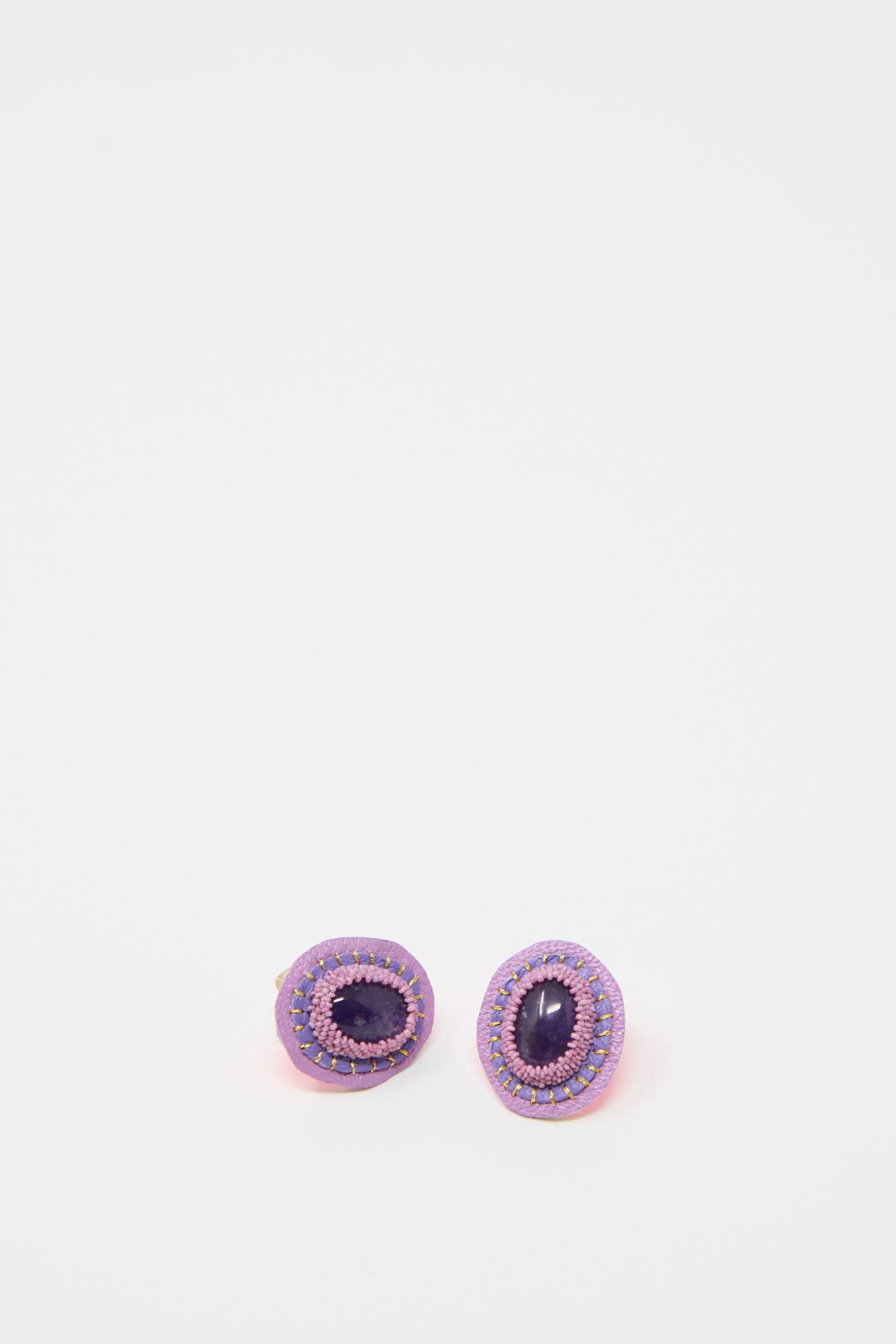 The "Oval Earrings in Amethyst" by Robin Mollicone, featuring pink and purple beads handcrafted into a unique design, are showcased against a white background.