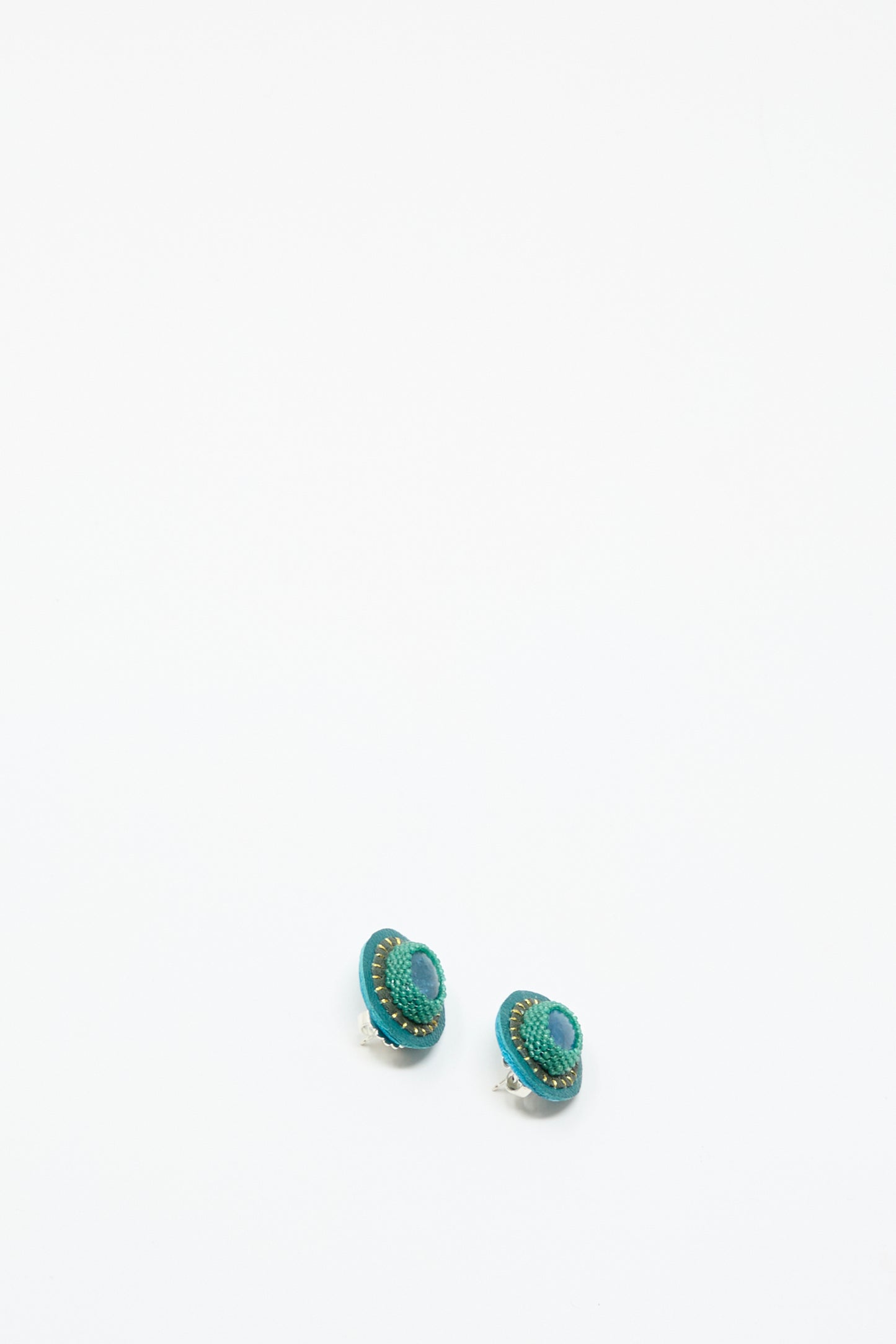 A pair of small, oval, teal and green handmade Robin Mollicone "Oval Earrings in Apatite" featuring a textured pattern, shown on a plain white background.