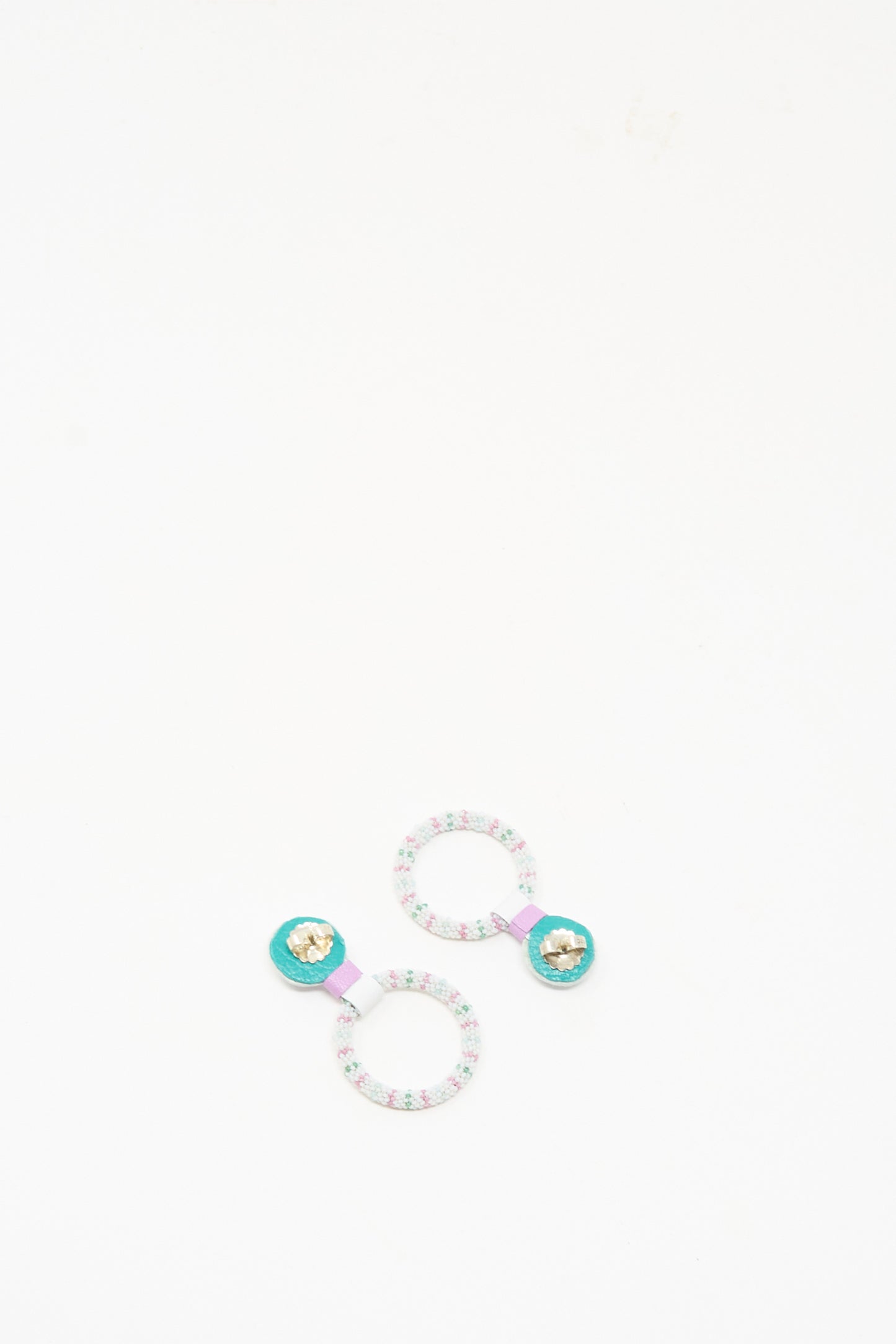 Two patterned hair ties with turquoise centers and gold star accents are displayed on a white background, capturing the vibrant, delicate style of Robin Mollicone’s Small Beaded Hoops in Rainbow Moonstone.