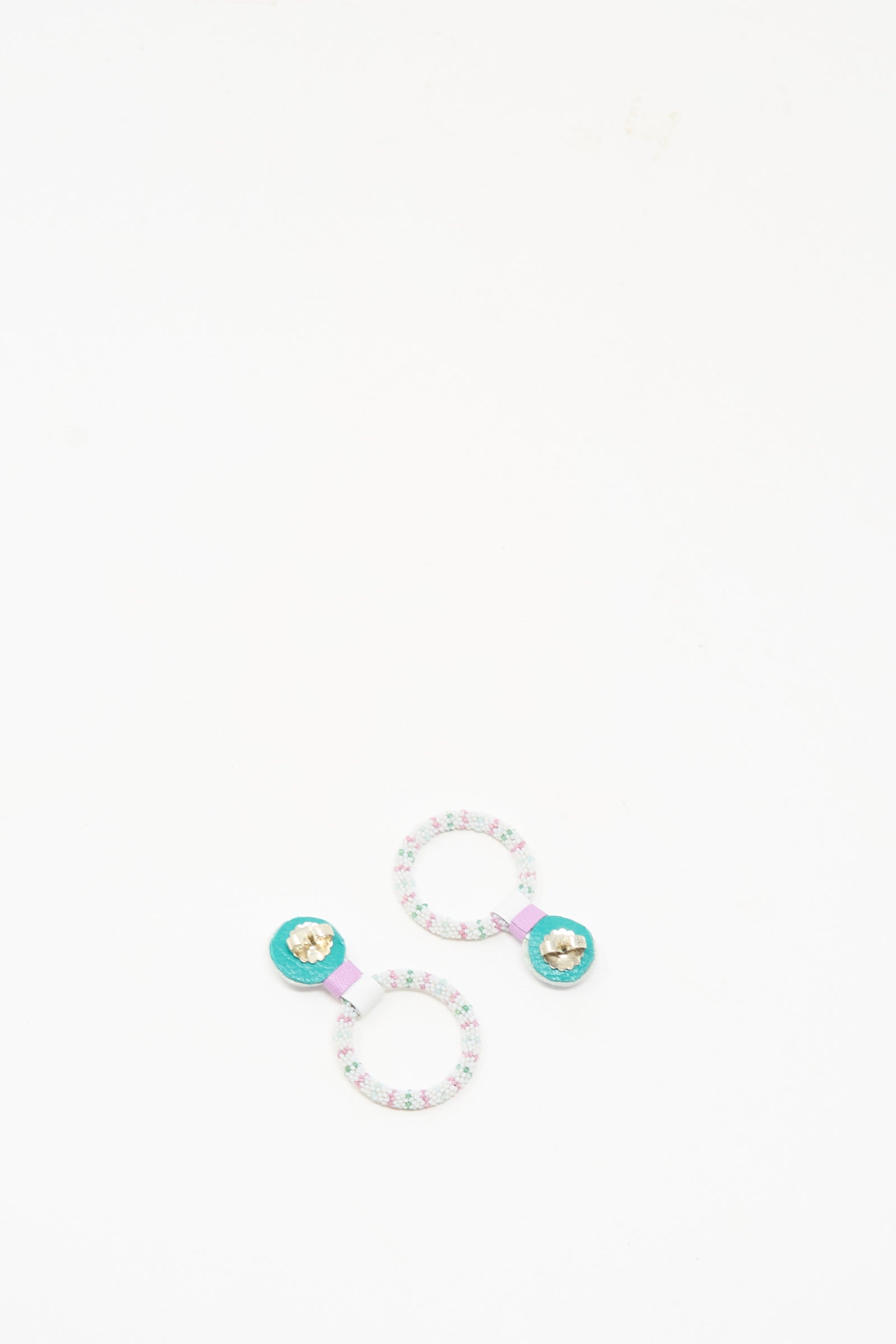Two patterned hair ties with turquoise centers and gold star accents are displayed on a white background, capturing the vibrant, delicate style of Robin Mollicone’s Small Beaded Hoops in Rainbow Moonstone.