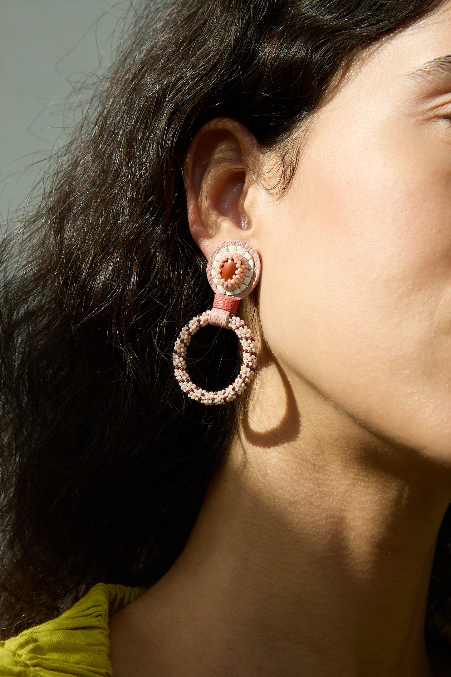 A close up of a woman's ear adorned with Robin Mollicone's Small Beaded Hoops in Red Jasper.