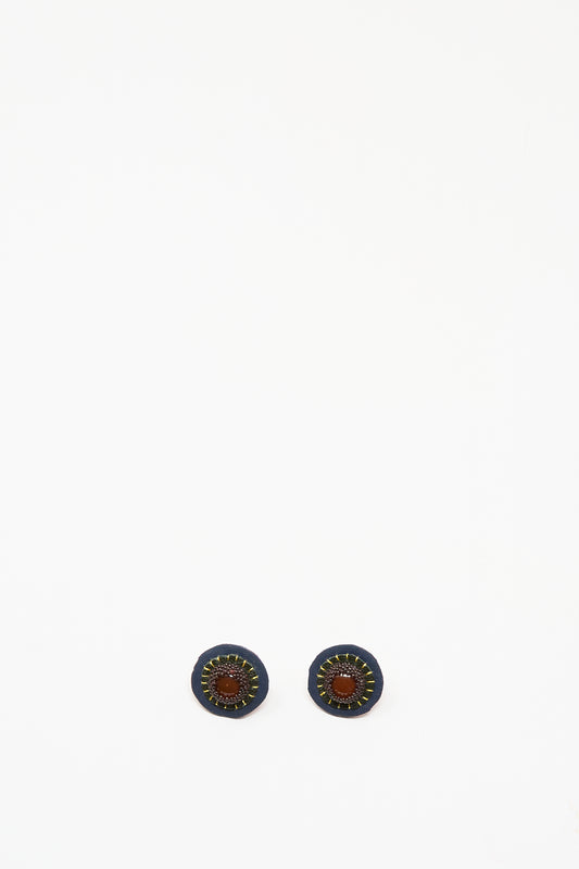 Robin Mollicone's Stud Earrings in Carnelian feature handmade round studs with a dark blue outer ring, brown leather center, and yellow stitched accents, shown on a white background.