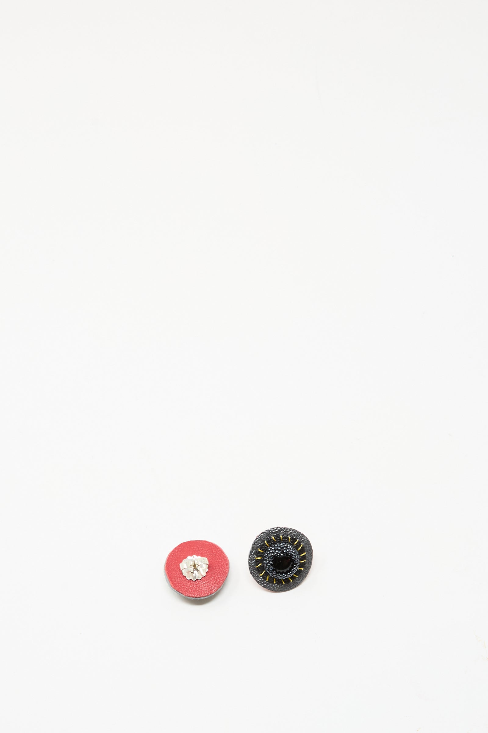 Two small, round Stud Earrings in Onyx by Robin Mollicone—a red one with a white center and a black one with a textured rim—are displayed side by side on a white background.