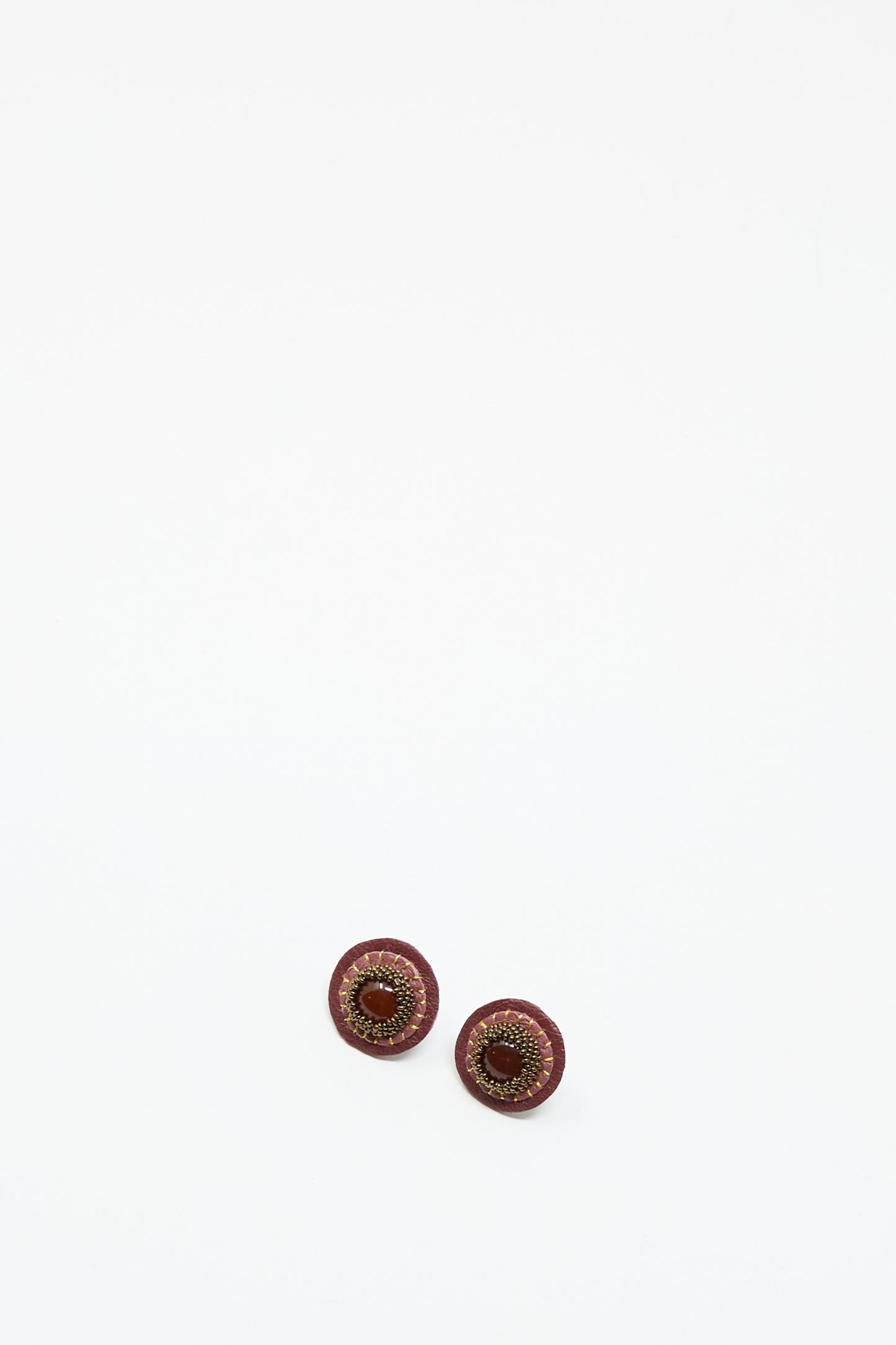 Two round, pink handmade stud earrings with carnelian by Robin Mollicone are displayed on a plain white background, resembling decorative buttons.